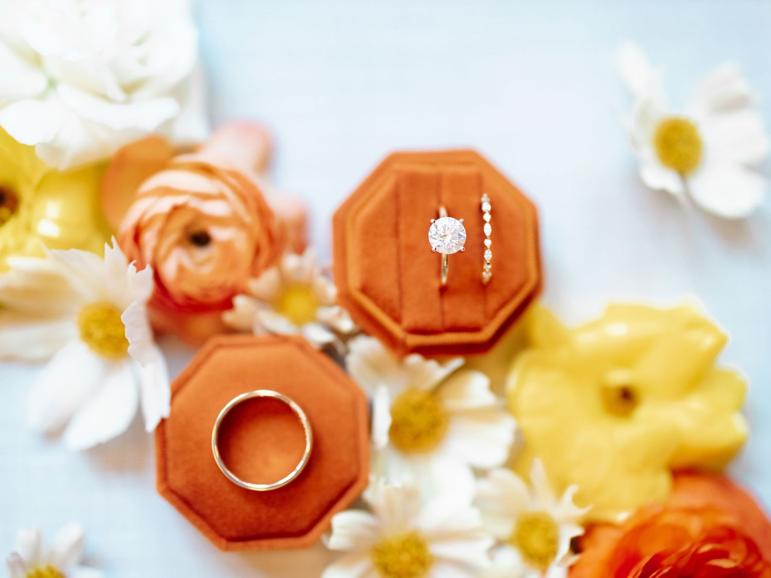 Diamond engagement ring in an orange velvet box surrounded by colorful orange, yellow, and white flowers.