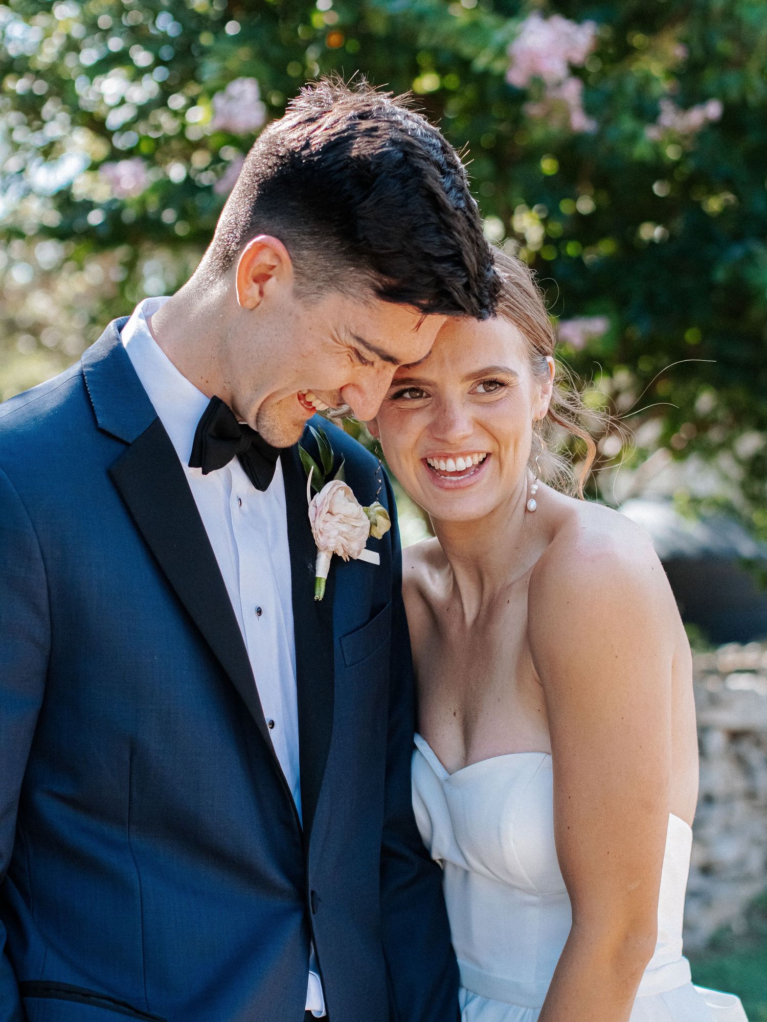 Happy bride and groom touching foreheads in sunny outdoor wedding portrait.