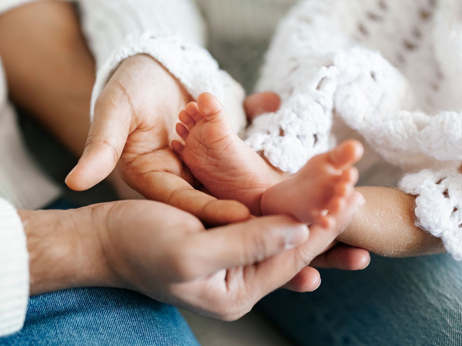 Parents tenderly holding newborn baby tiny feet in their hands during intimate newborn photo session.