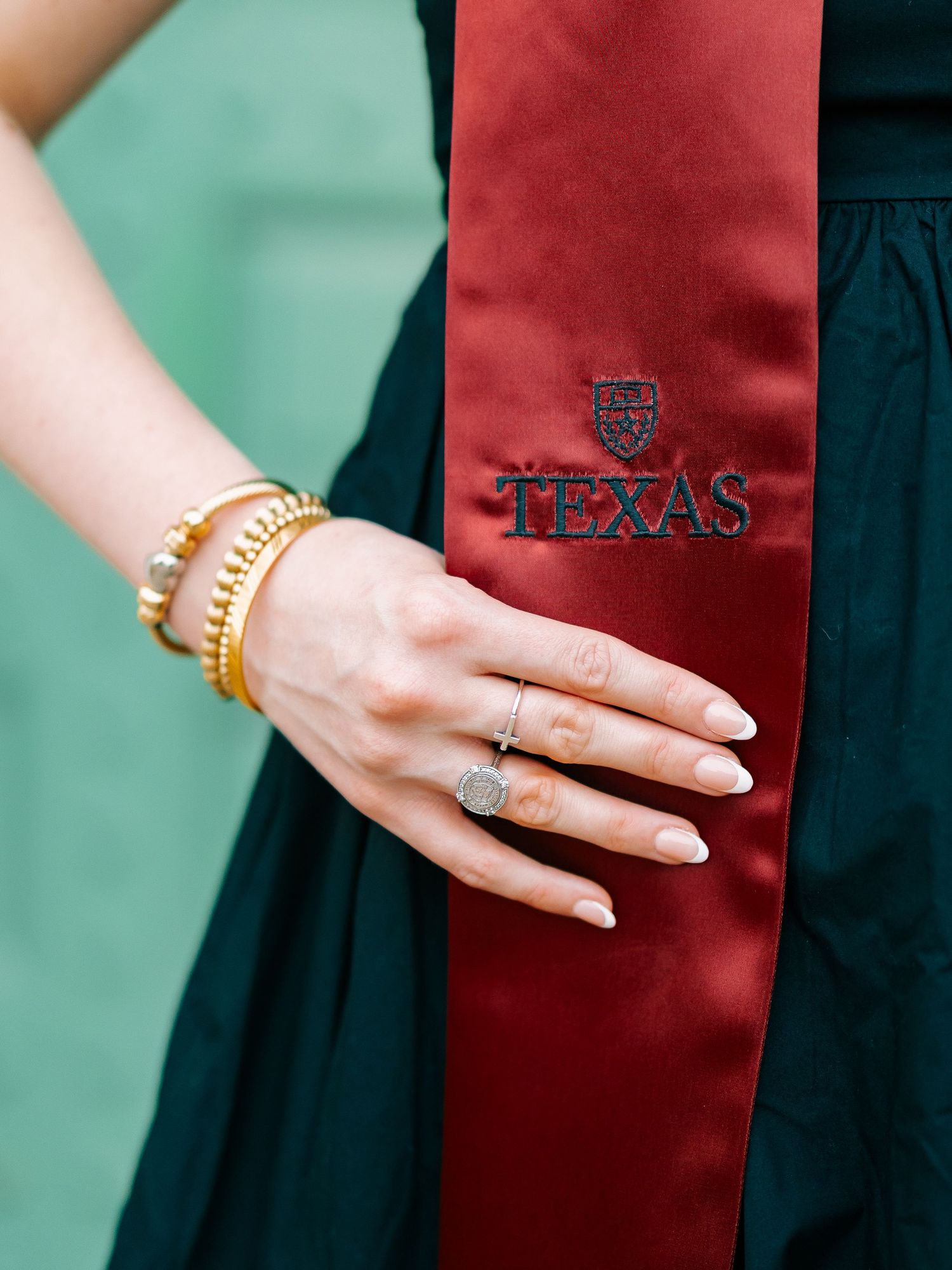 Close-up of a hand wearing a diamond ring and gold bracelets resting on a maroon University of Texas graduation stole.