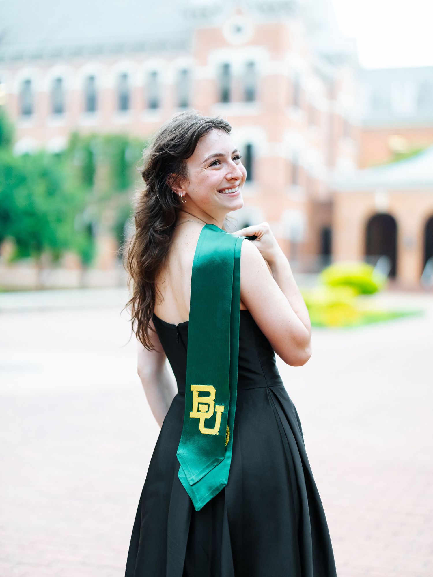 Smiling Baylor University graduate poses in black dress with green BU graduation sash.
