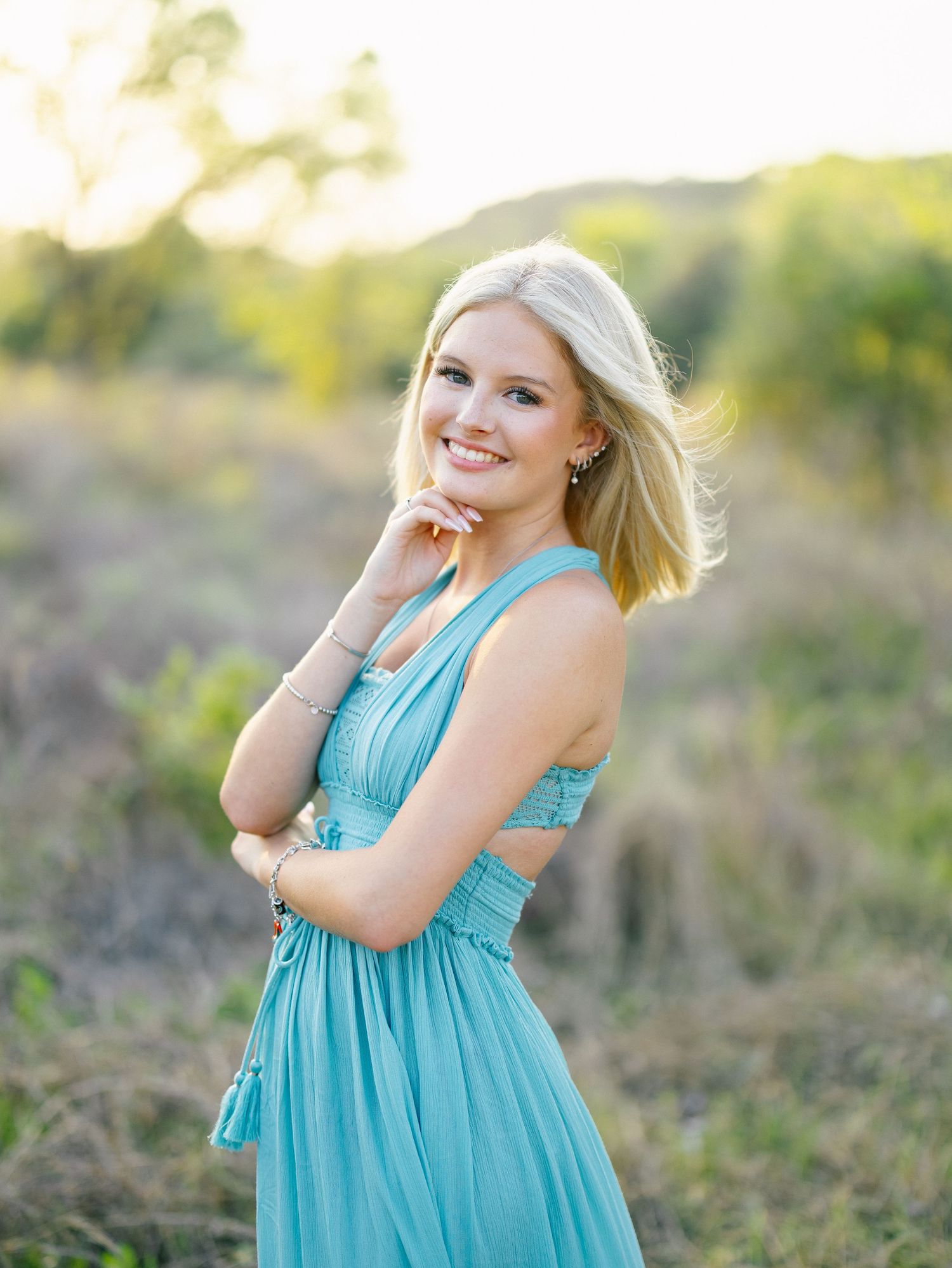 Smiling blonde woman in teal dress posing outdoors in golden hour light.