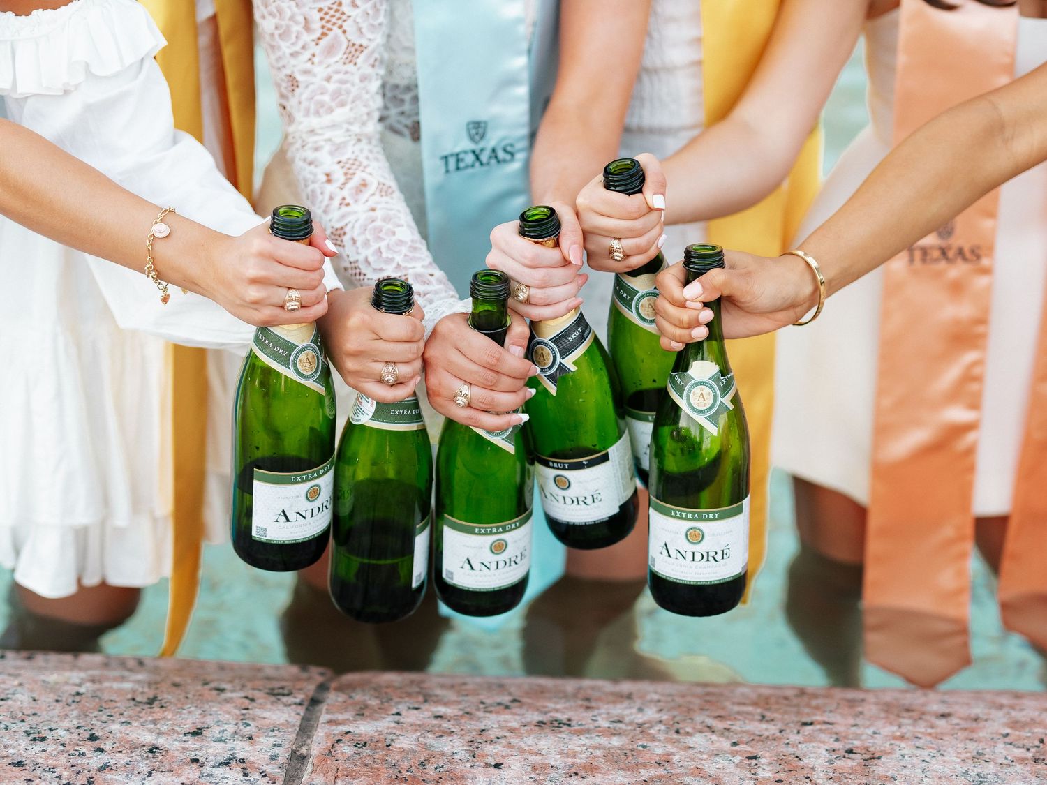 Women in white dresses holding Antsee champagne bottles together at a Texas celebration event.