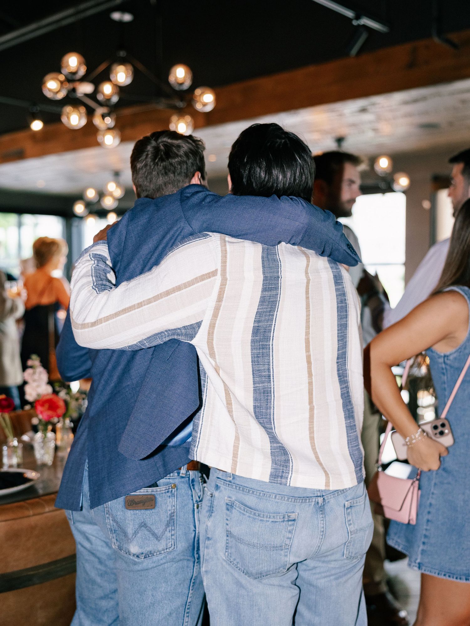 Two friends share a warm hug at an indoor wedding rehearsal dinner party.