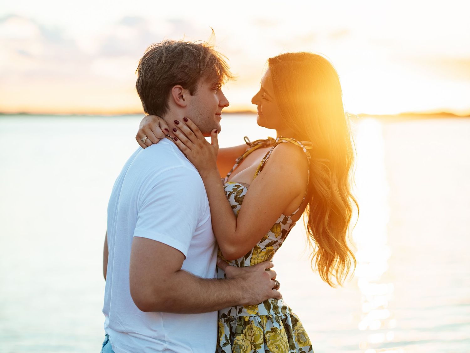 Romantic couple holding each other close near water during golden hour sunset.