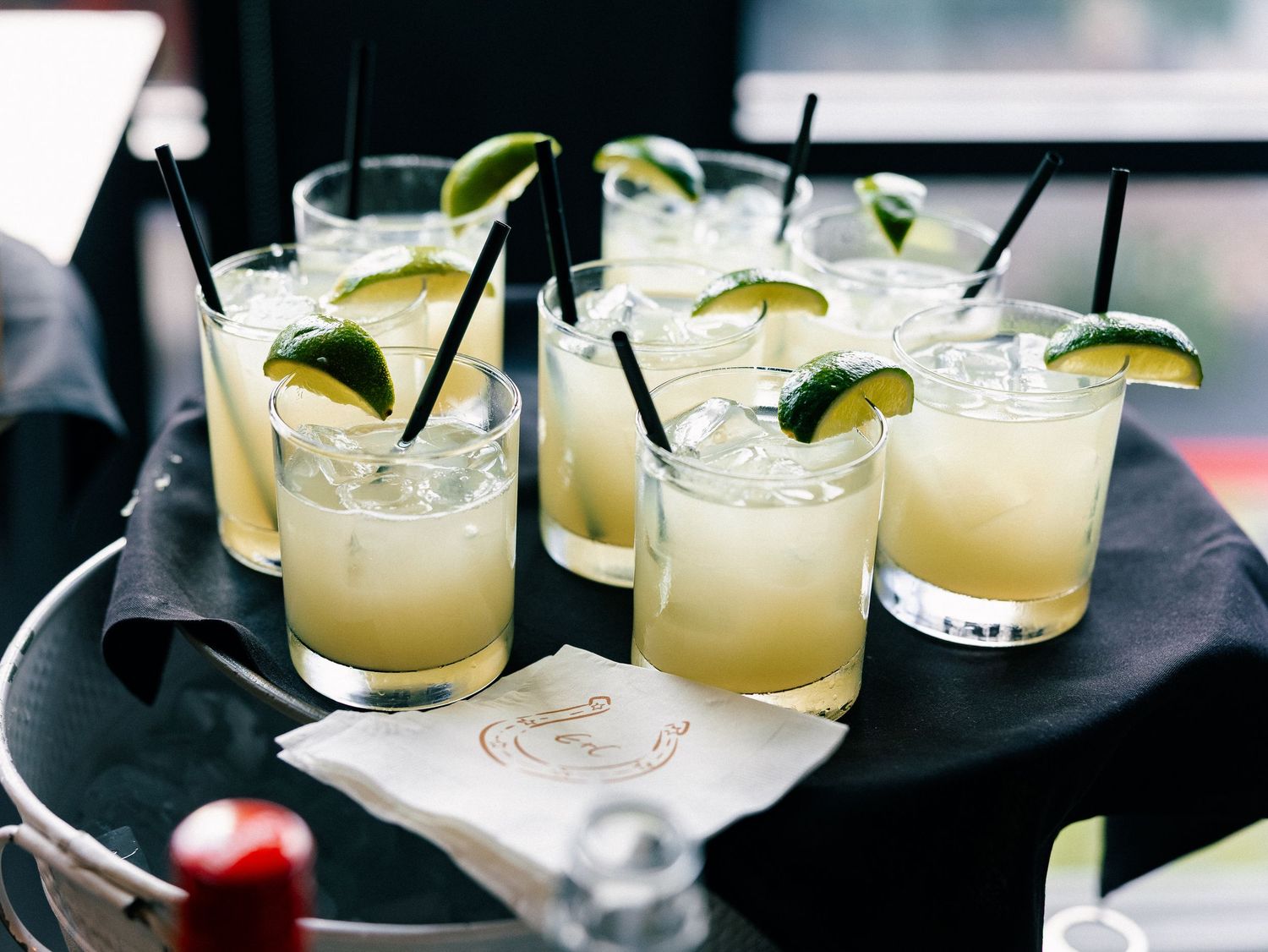 Six margarita cocktails with lime wedges and black straws on a silver tray, perfect for a party gathering.