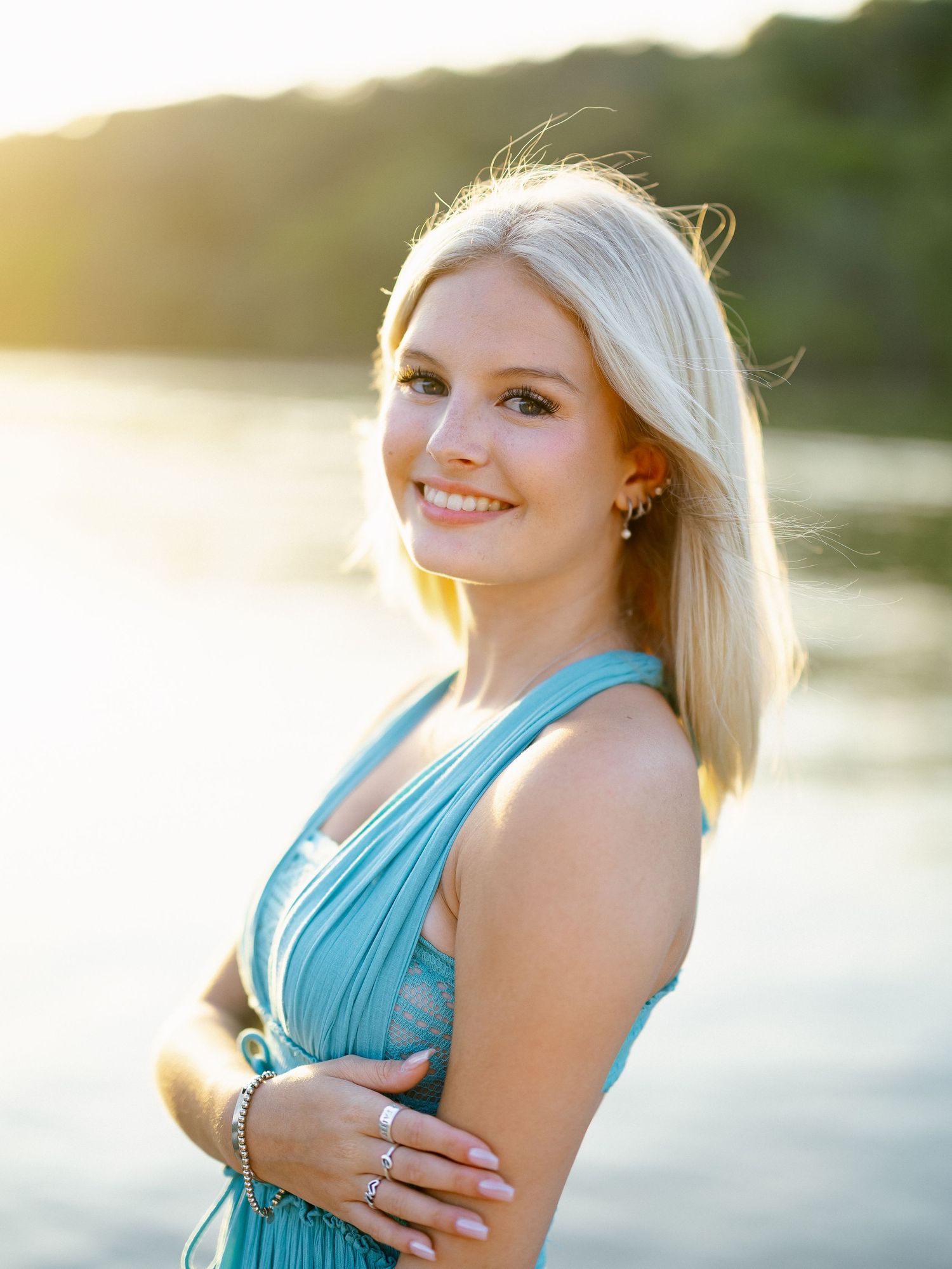 Close-up of a smiling blonde teen in a teal halter dress with golden sunset reflecting off a lake.