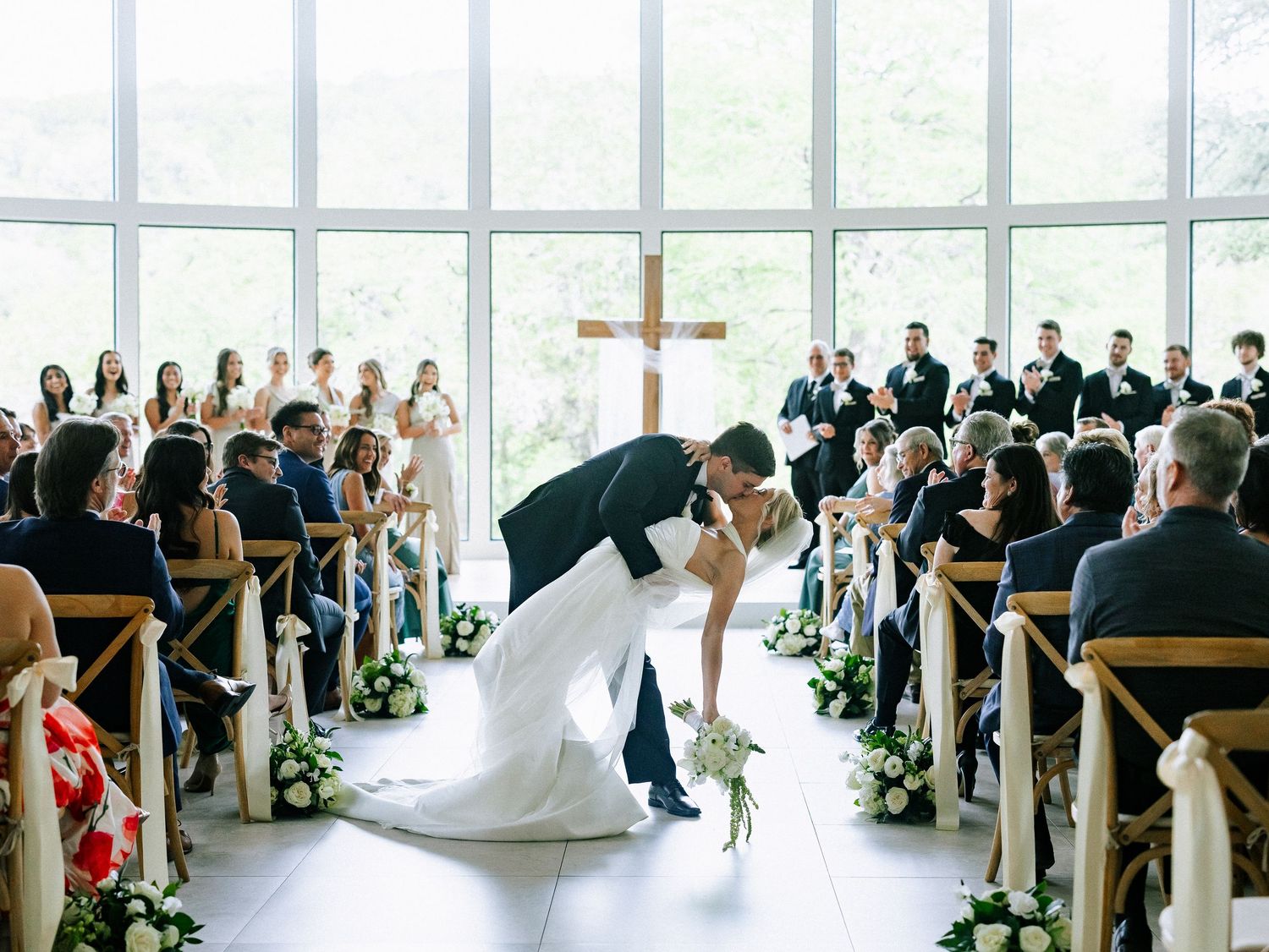 Bride and groom share a romantic dip kiss at the altar during their wedding ceremony in a sunlit chapel.