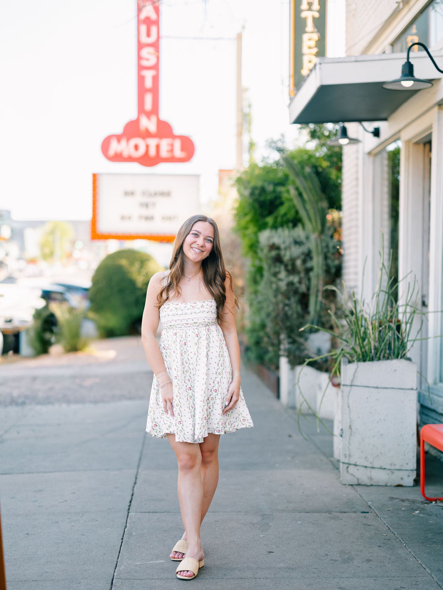 Smiling woman in white sundress posing outside Austin Motel on sunny day.