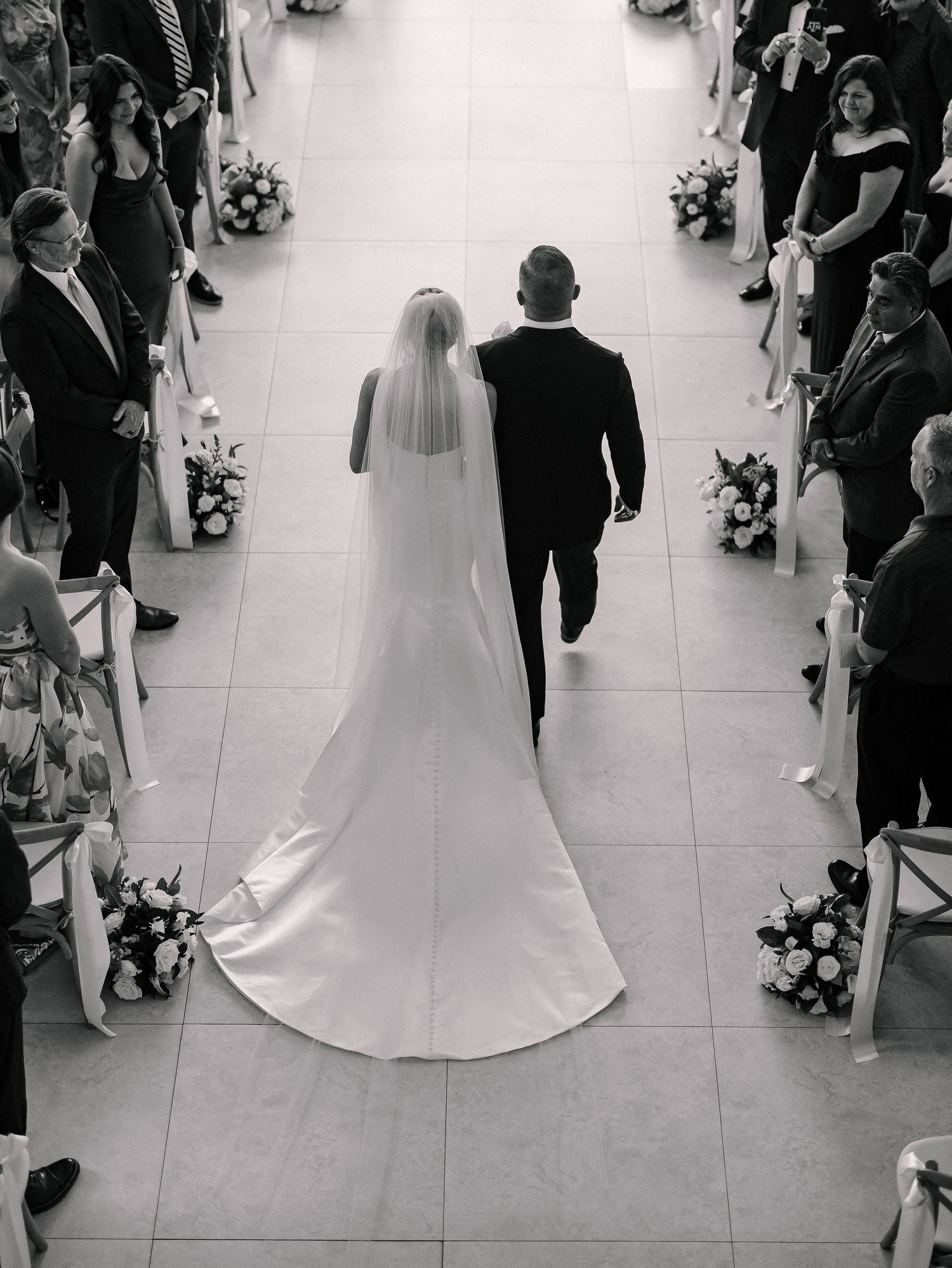 Aerial black and white photo of bride and groom walking down wedding aisle.