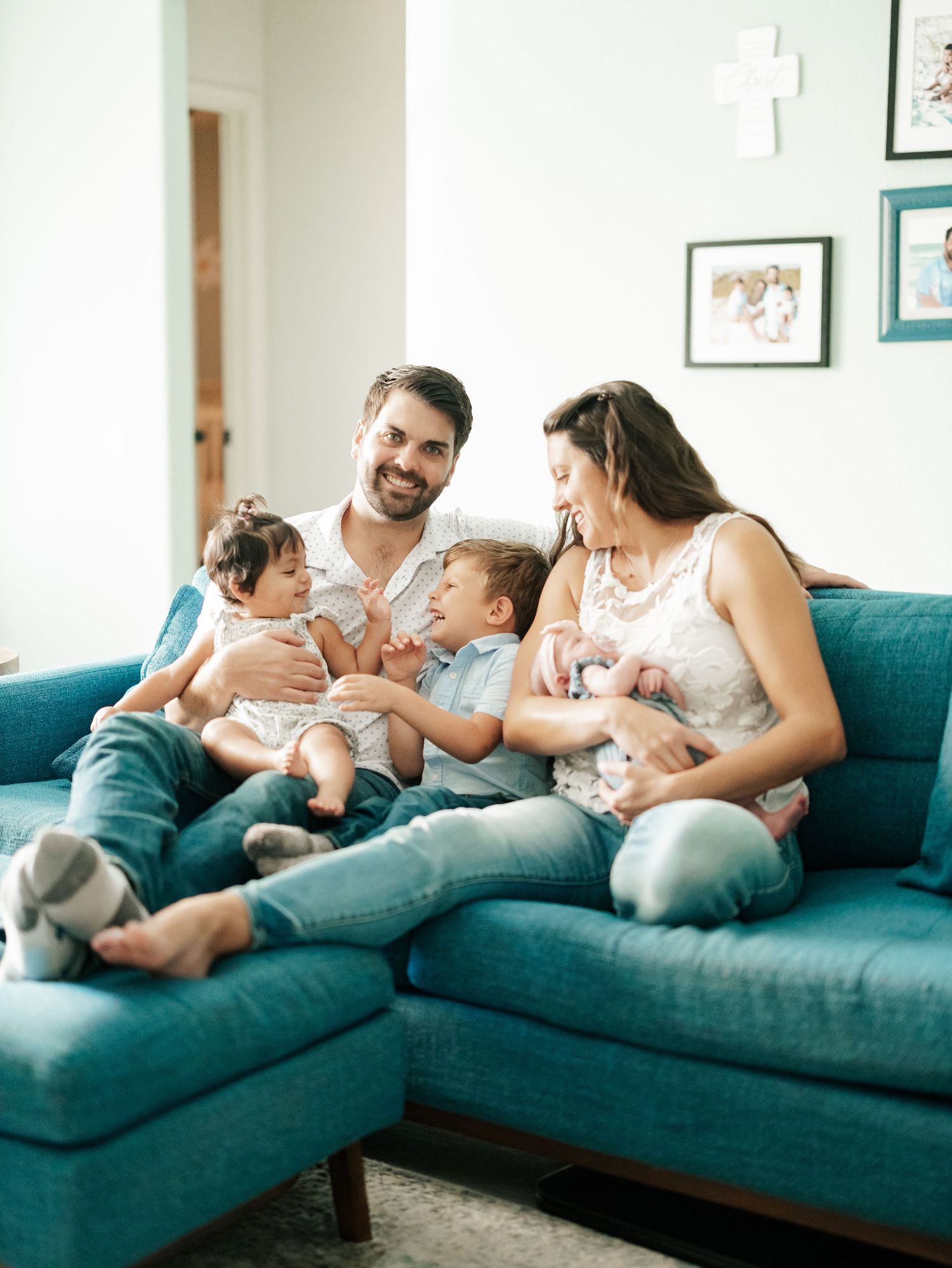 Happy family of four relaxes together on teal couch in bright living room.