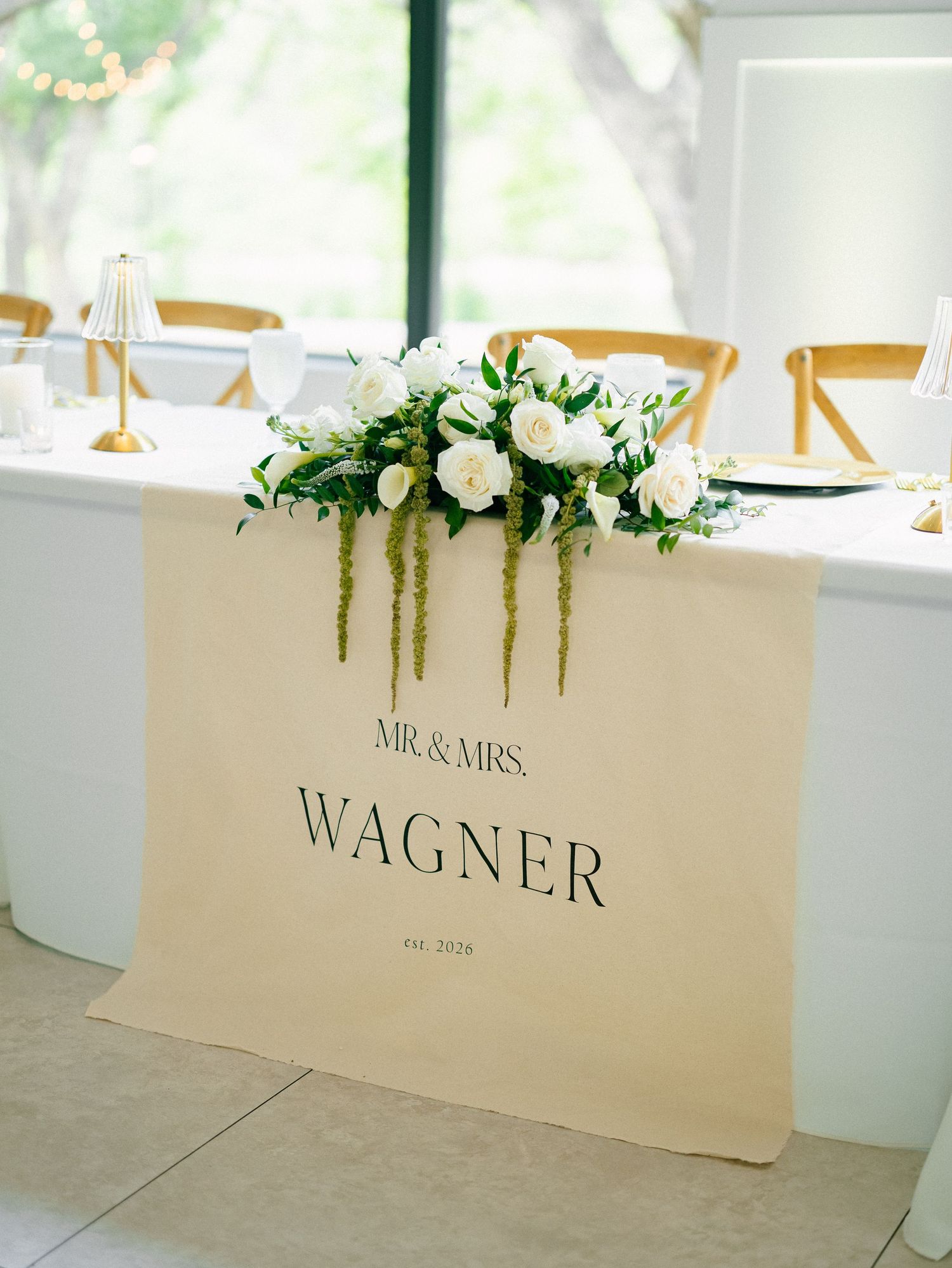 Elegant wedding sweetheart table with Mr. & Mrs. Wagner sign, white roses, and greenery floral arrangement.