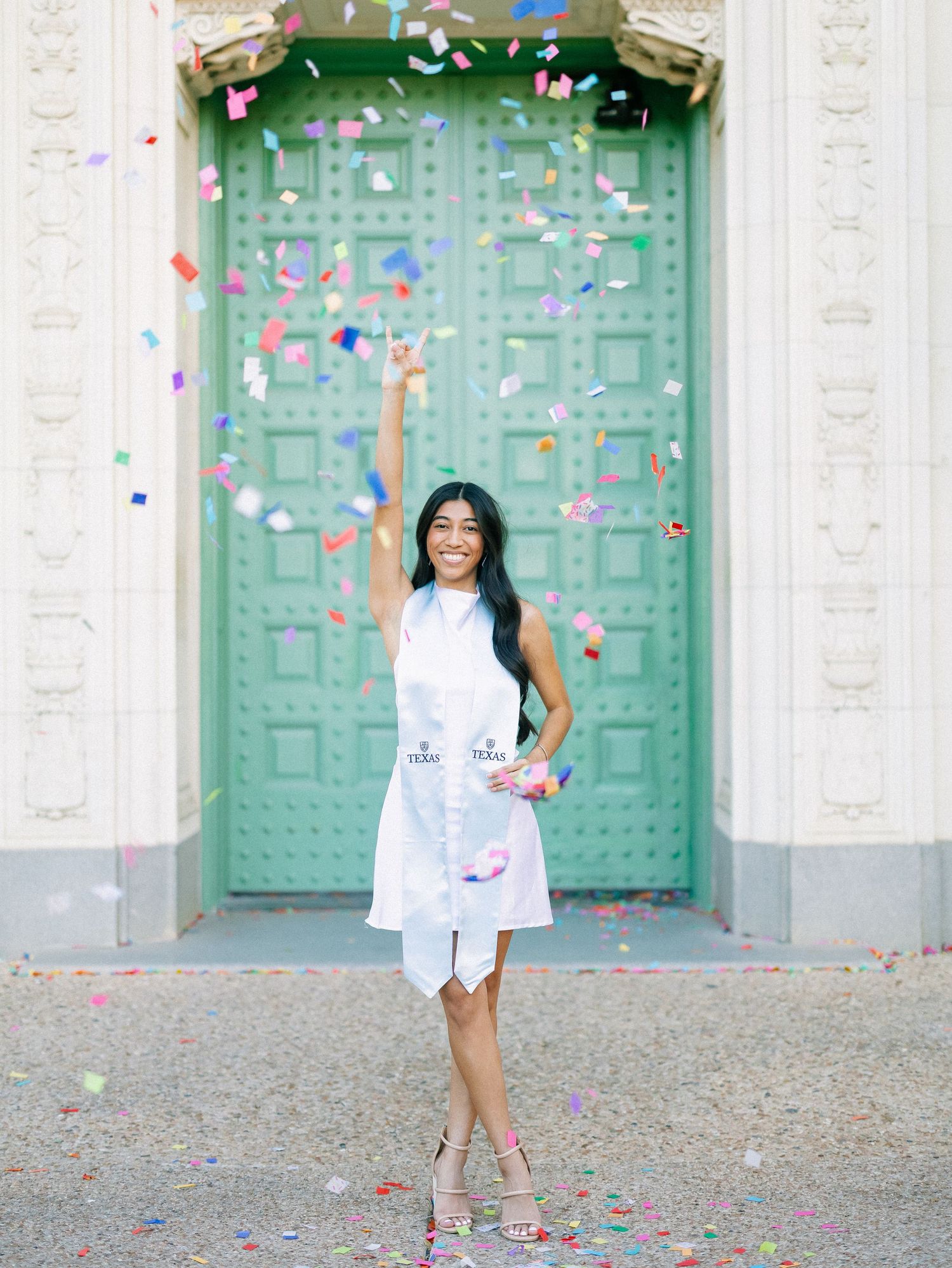 Woman in white dress celebrating with colorful confetti in front of a green ornate door.