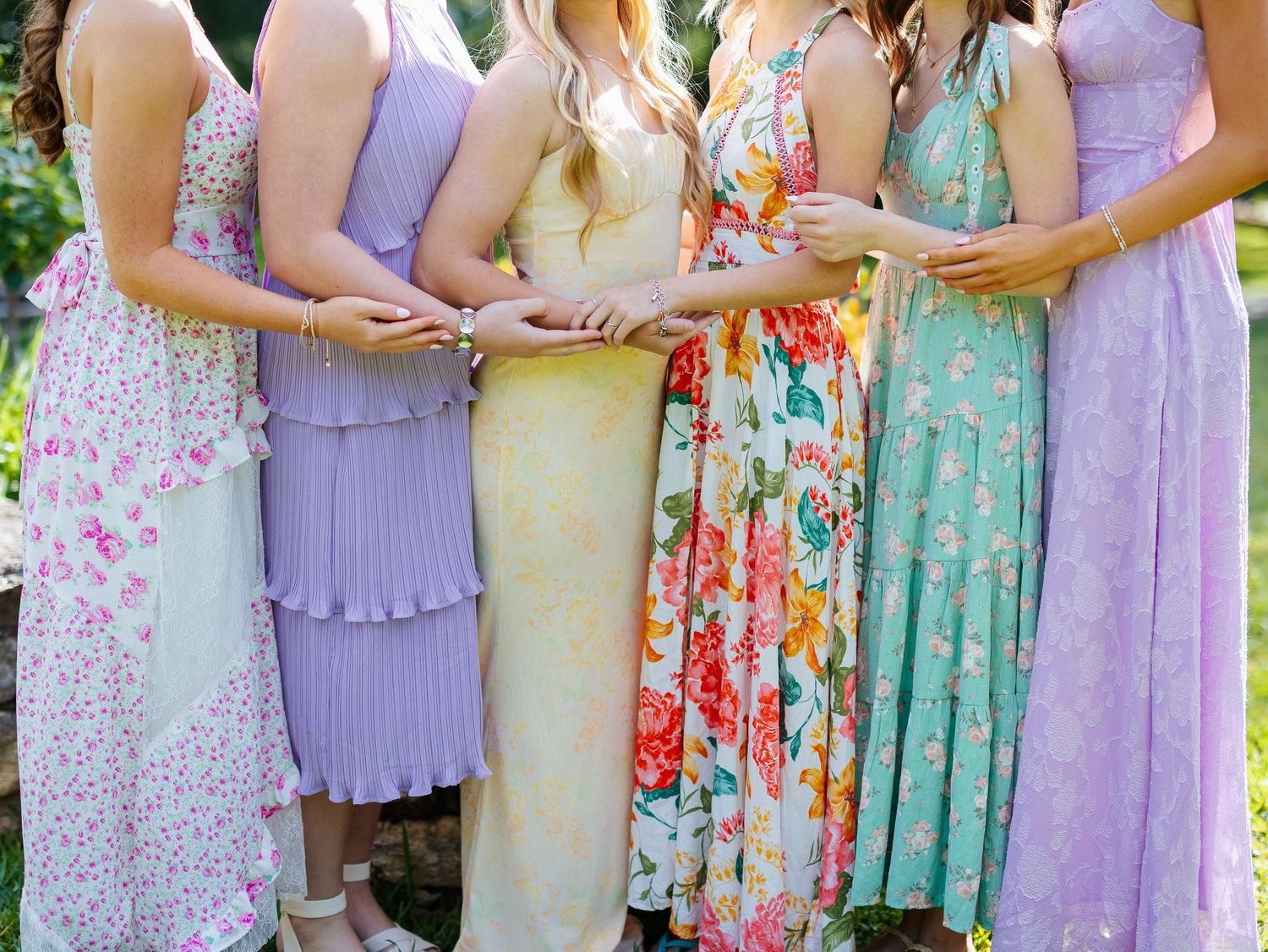 Group of bridesmaids in colorful pastel floral and lavender dresses standing together outdoors.