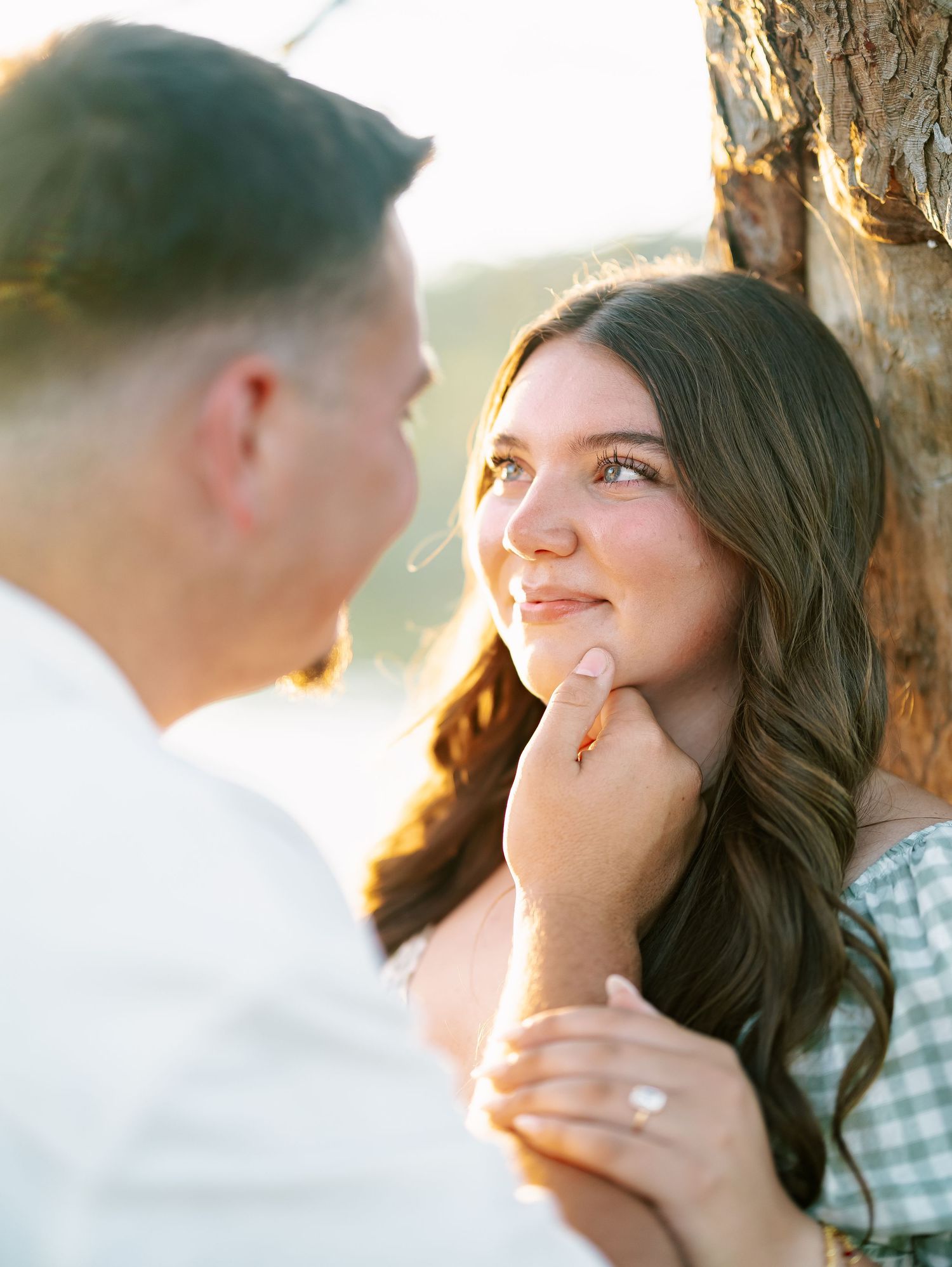Close-up of engaged couple sharing an intimate moment with diamond ring visible near tree.