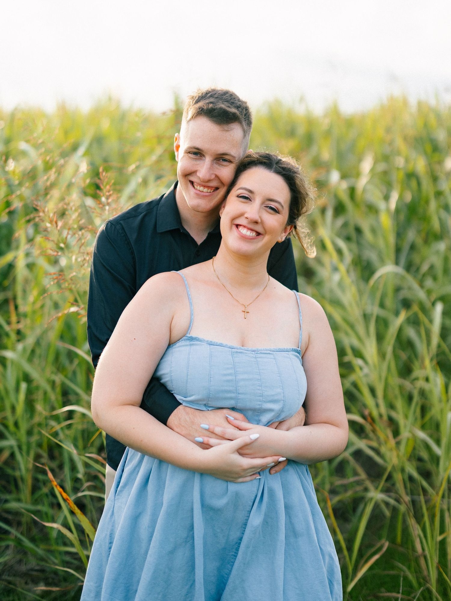 Smiling couple posing together in a lush green cornfield at golden hour.