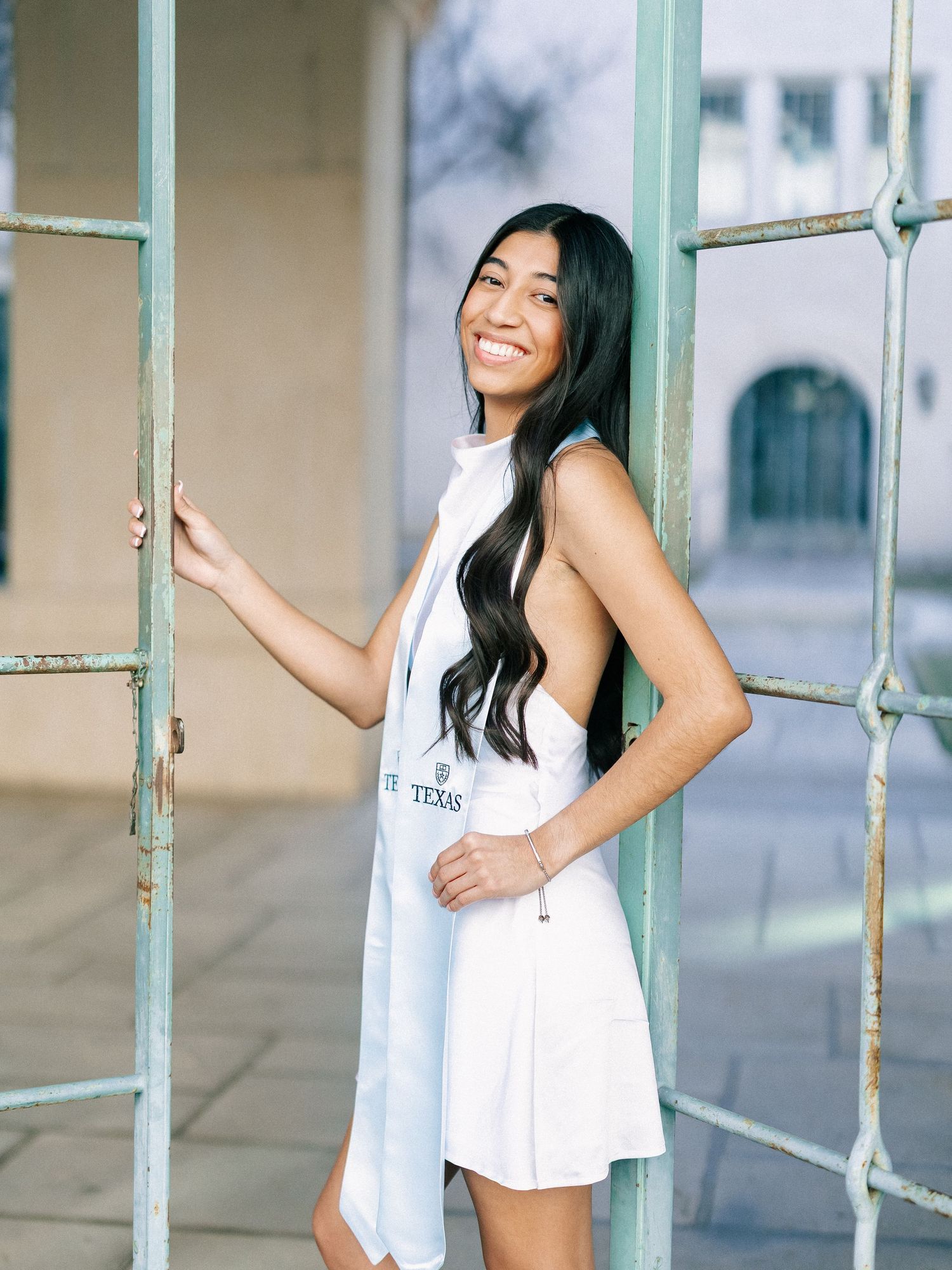 Young woman in white dress smiling and posing by vintage green metal doors in an outdoor setting.