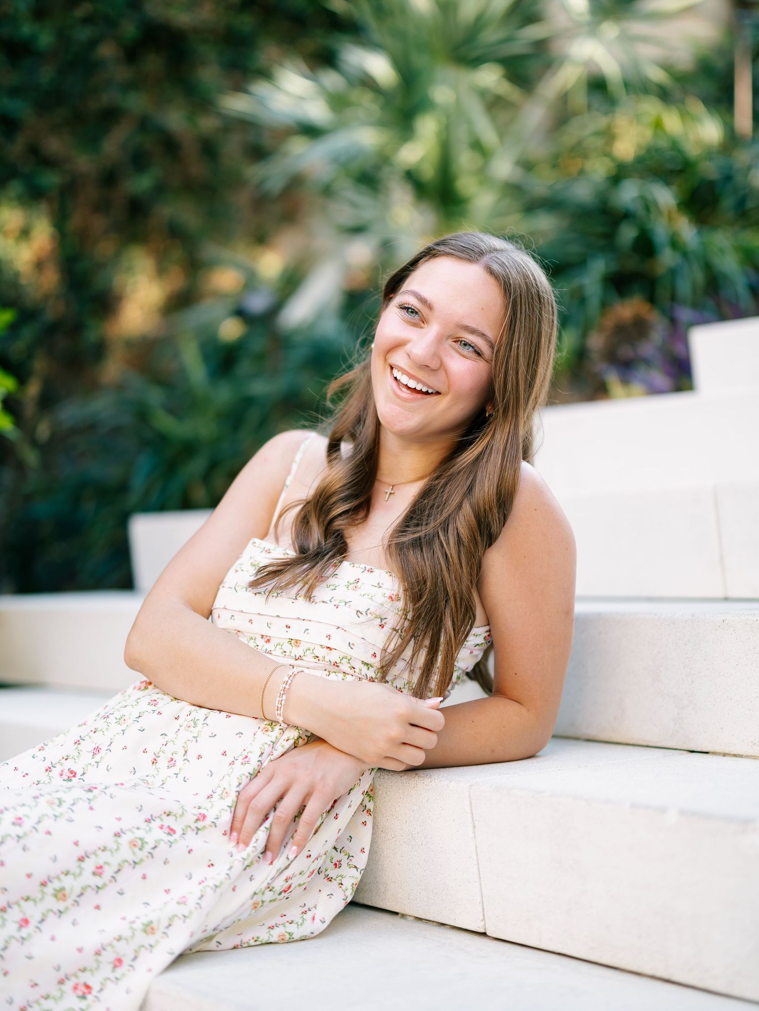 Young woman in floral dress laughing while seated on white outdoor steps.