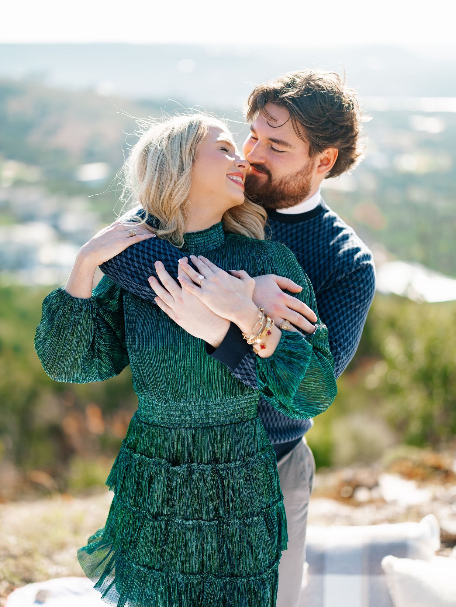 Couple sharing a tender almost-kiss while embracing outdoors in green and navy sweaters.