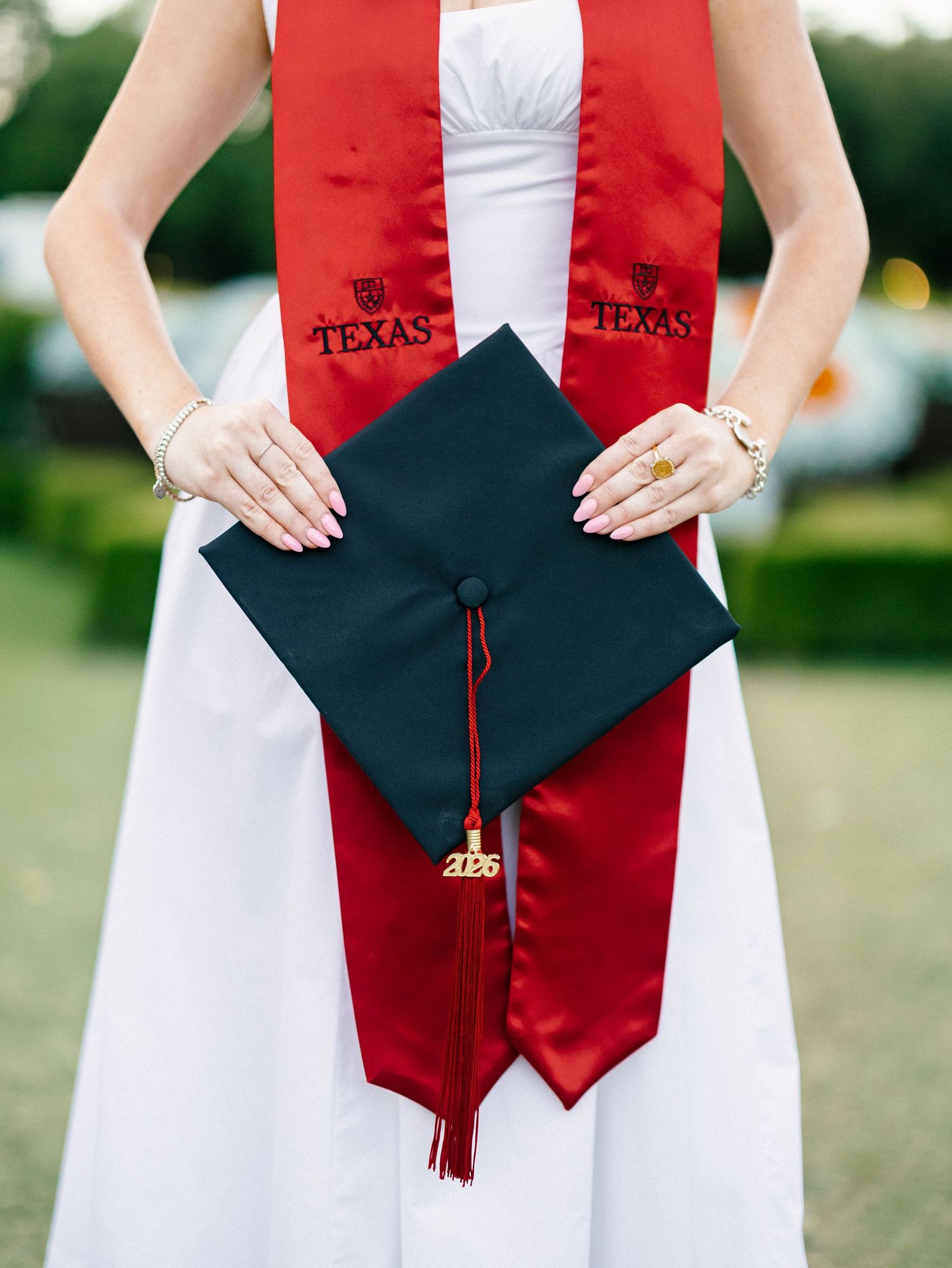 University of Texas graduate holding black mortarboard cap with red tassel and Texas sash in white dress.