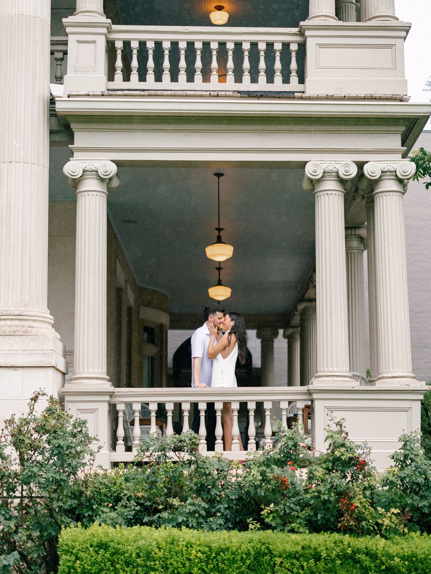 Couple sharing a tender kiss on the upper balcony of a stately historic mansion with white columns.