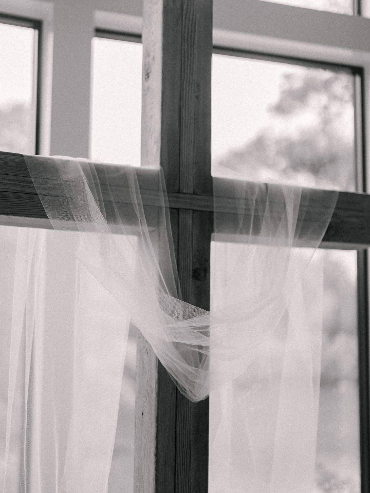 Delicate white bridal veil draped over rustic wooden window frame in black and white wedding photo.