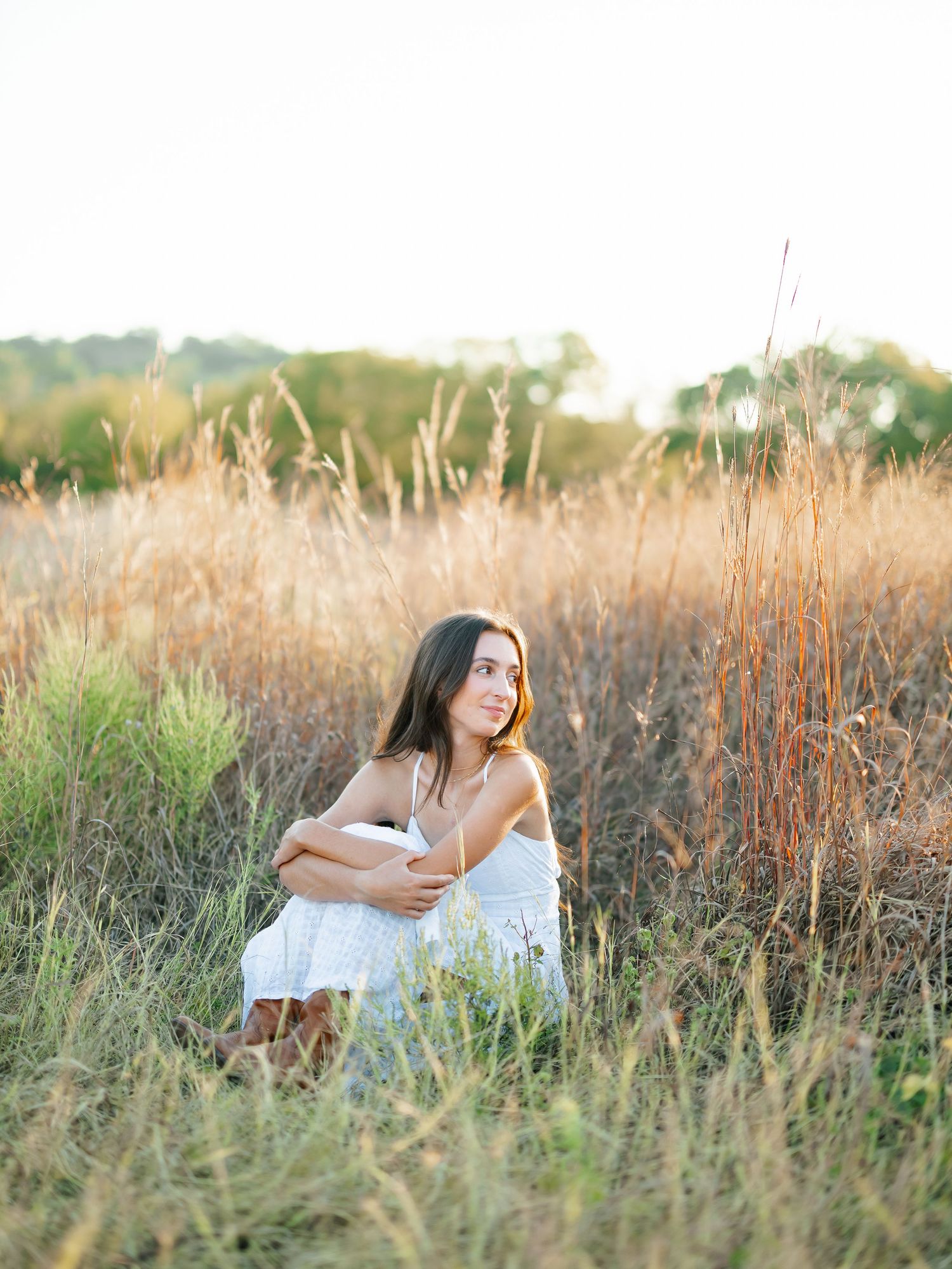 Young woman in white dress sitting in golden field grass during sunset golden hour photography.