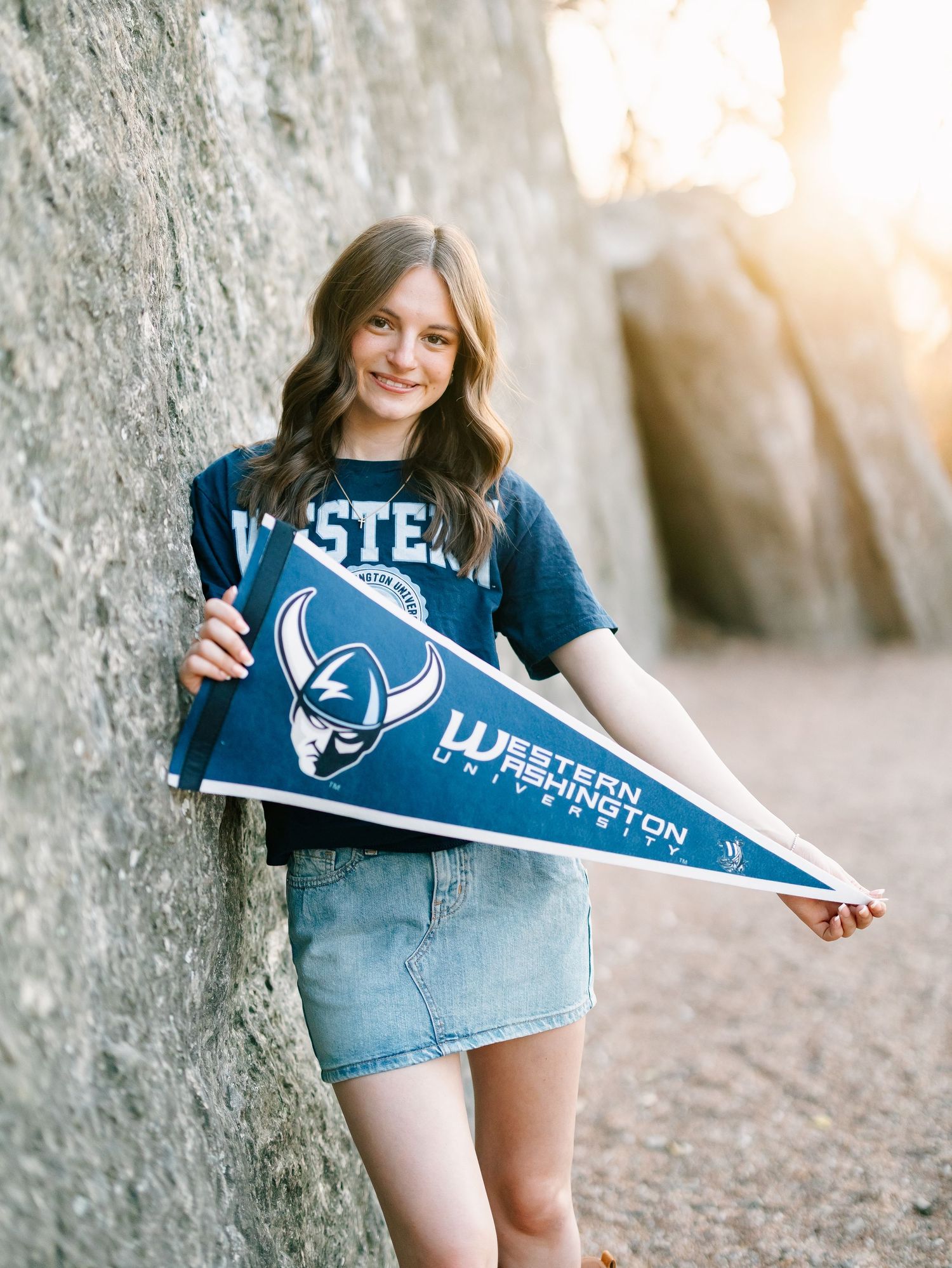 Smiling teen holding Western Washington University pennant leaning against rock wall.