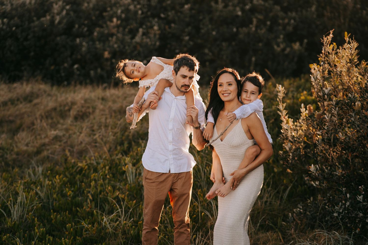 A happy family of four posing together in a sunlit meadow during golden hour.