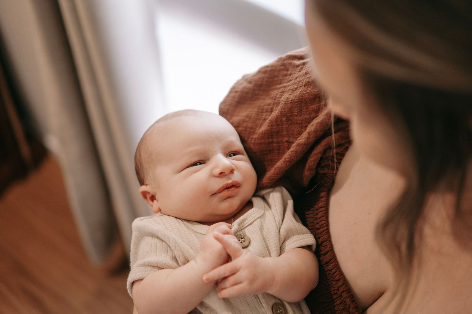 A newborn baby with a slight smile being cradled in a mother's arms indoors.