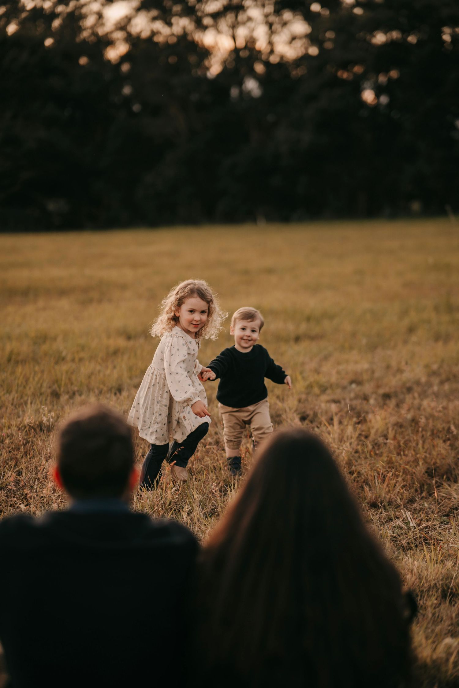 Two young children running toward their parents across a golden sunset meadow.