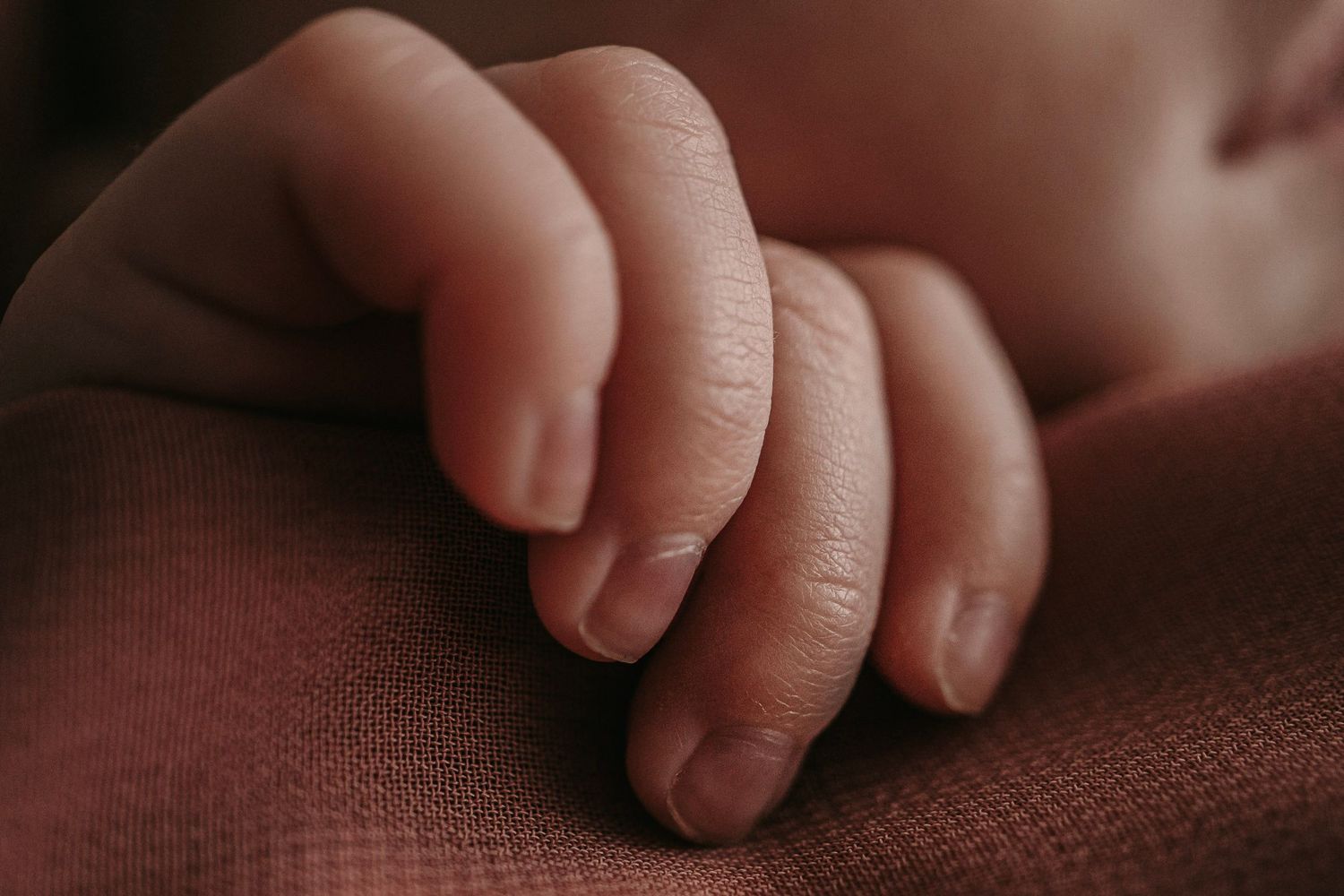 Close-up of a newborn baby's tiny delicate hand resting on a soft pink knit blanket.