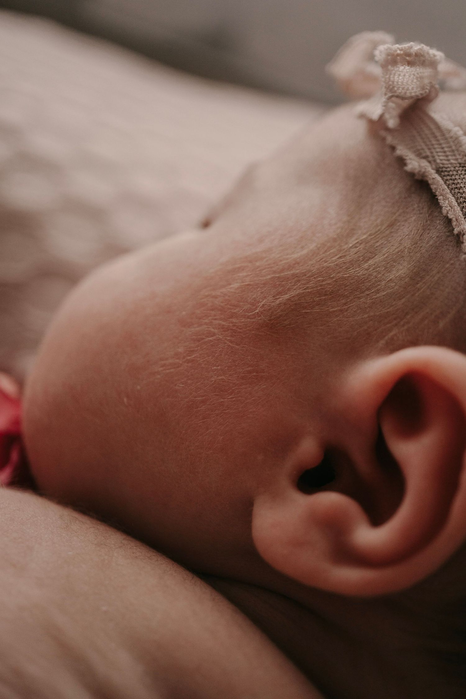 Close-up of a sleeping newborn baby's ear and head with a delicate pink floral headband.