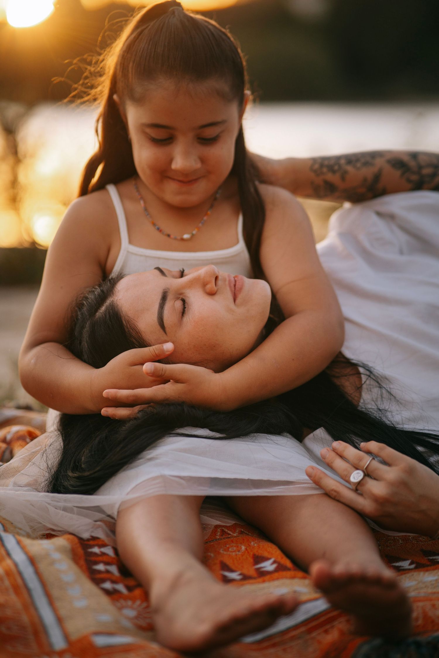Young girl tenderly cradling mothers head in her lap during golden hour outdoors.