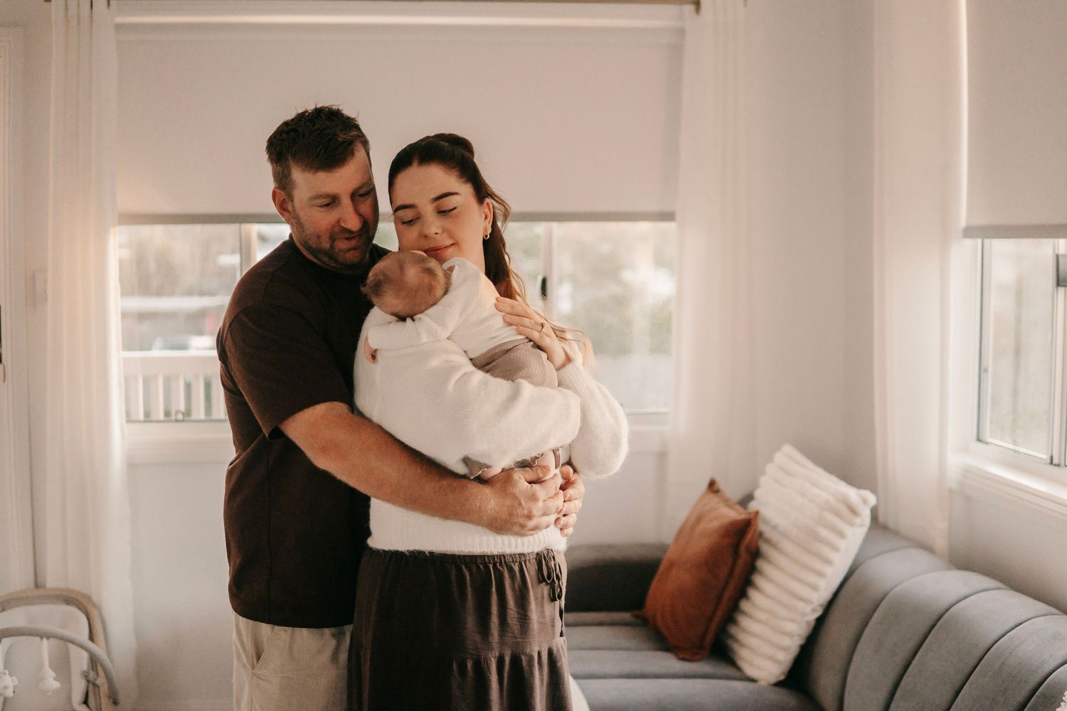 Happy couple embracing while mother holds newborn baby in bright cozy living room.