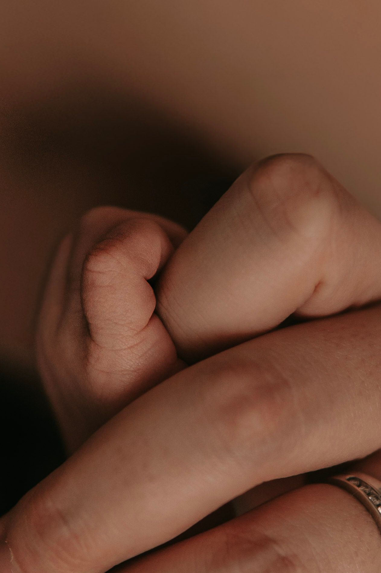 A newborn baby's tiny fist resting gently on an adult's fingers, showcasing the delicate bond between parent and child.