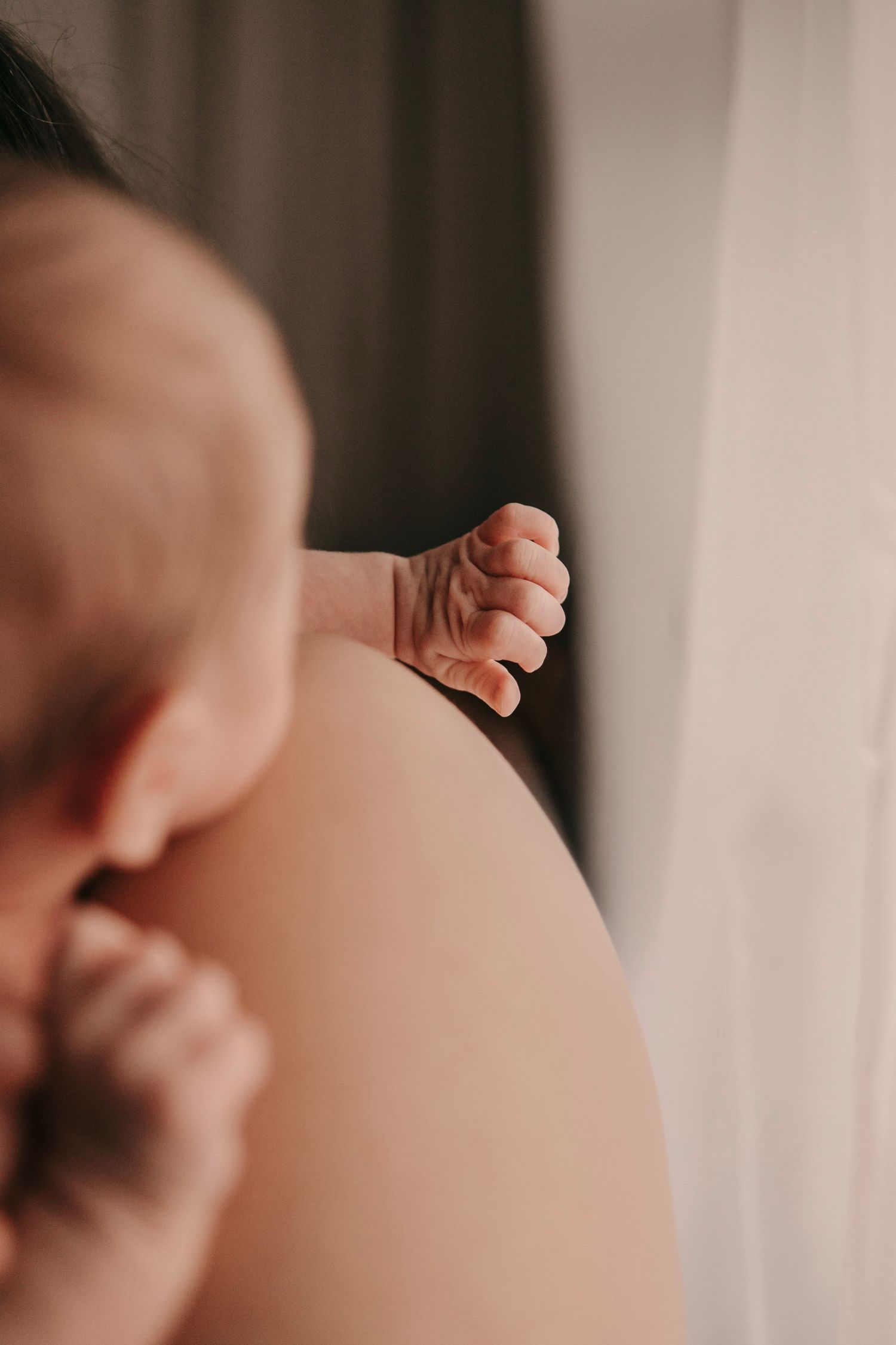 Close-up of a newborn baby's tiny hand resting on a parent's shoulder during a tender bonding moment.