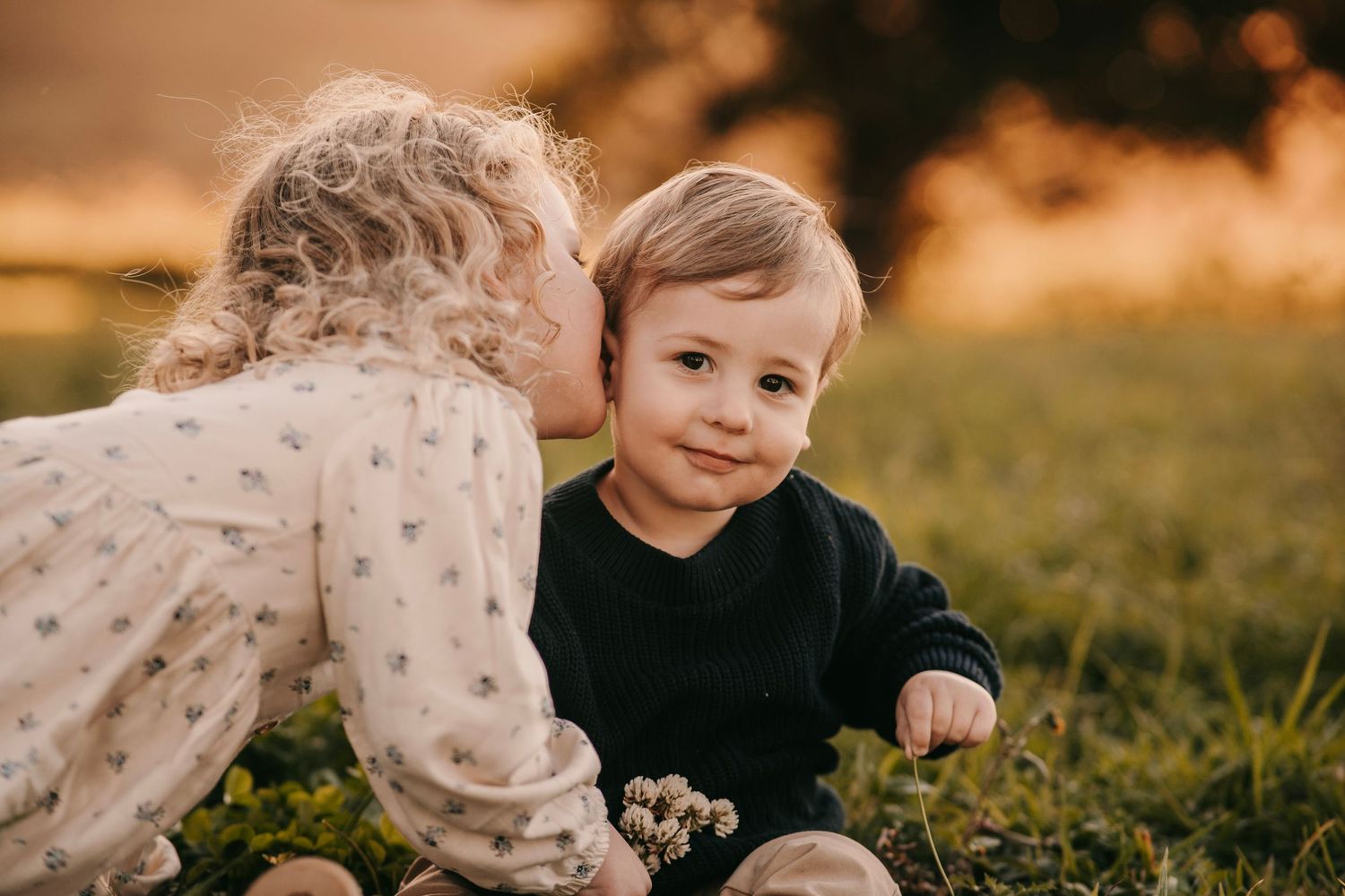 Sweet young girl giving her baby brother a gentle kiss on the cheek outdoors.