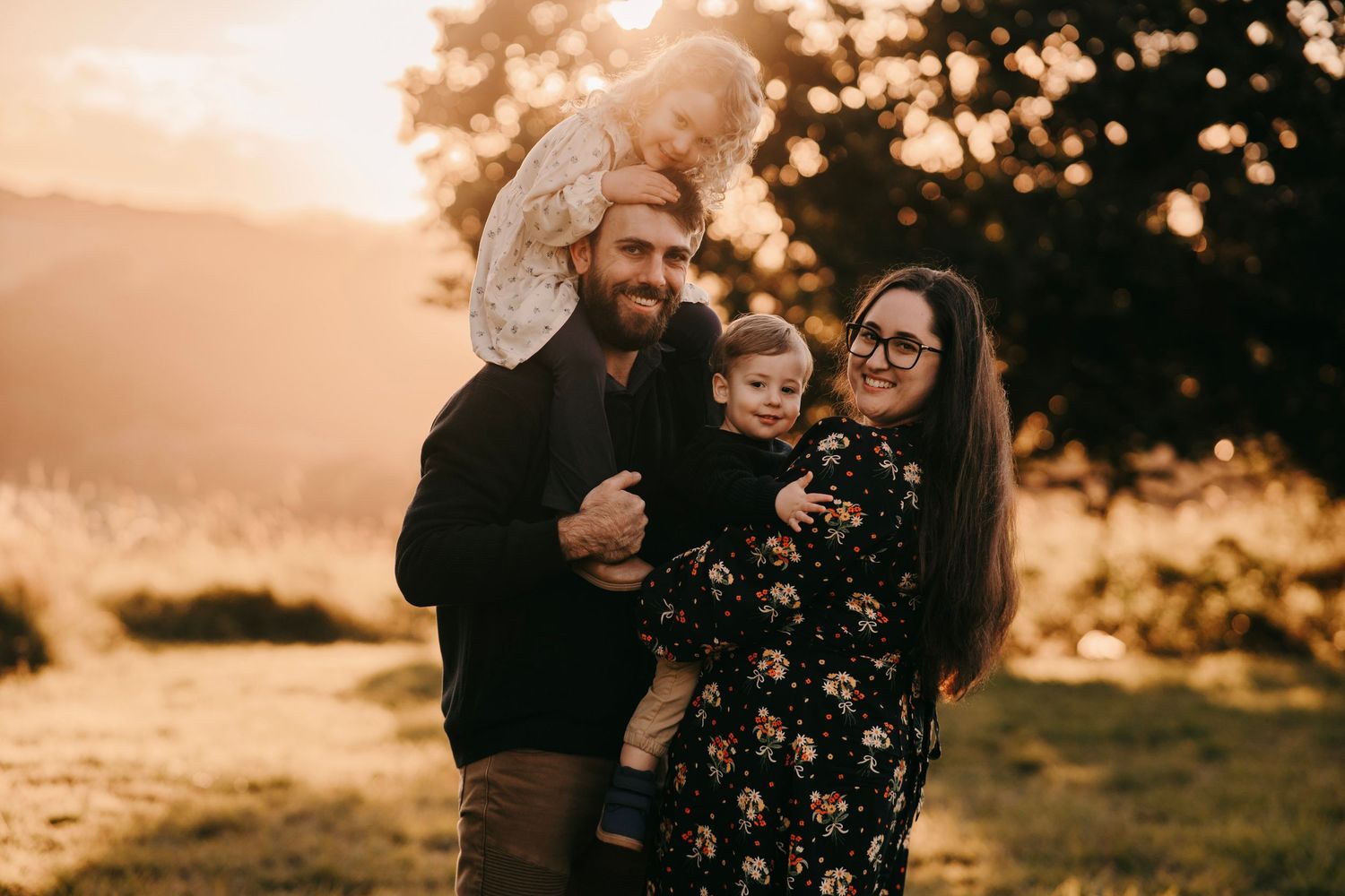 Happy family of four posing together at golden hour in a scenic outdoor field.