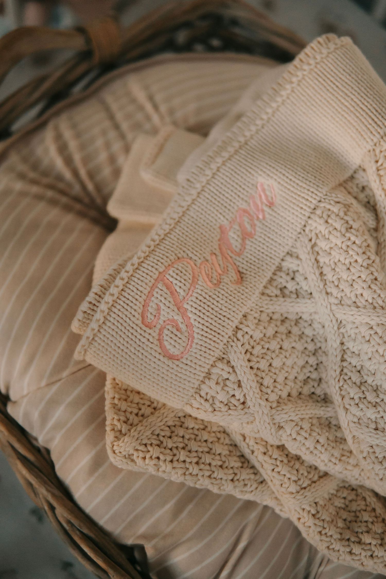 A personalized beige knit baby blanket embroidered with the name Peyton in a wicker basket.