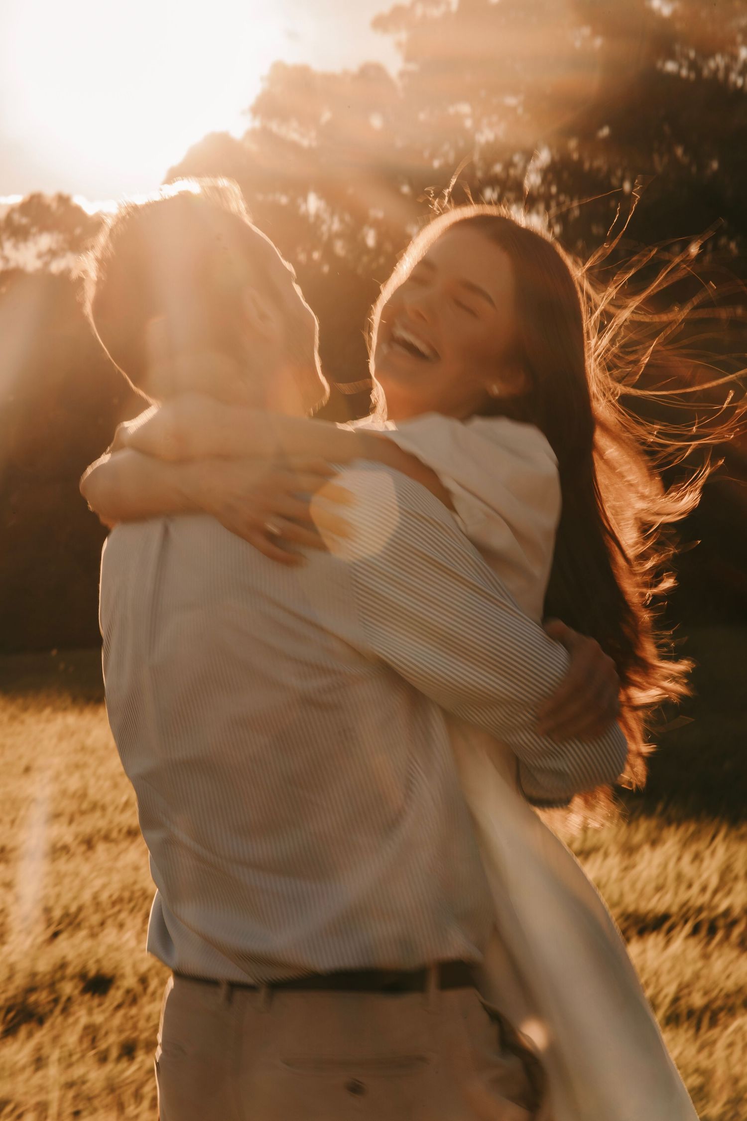 A joyful couple laughing and embracing in a golden sunlit field at sunset.