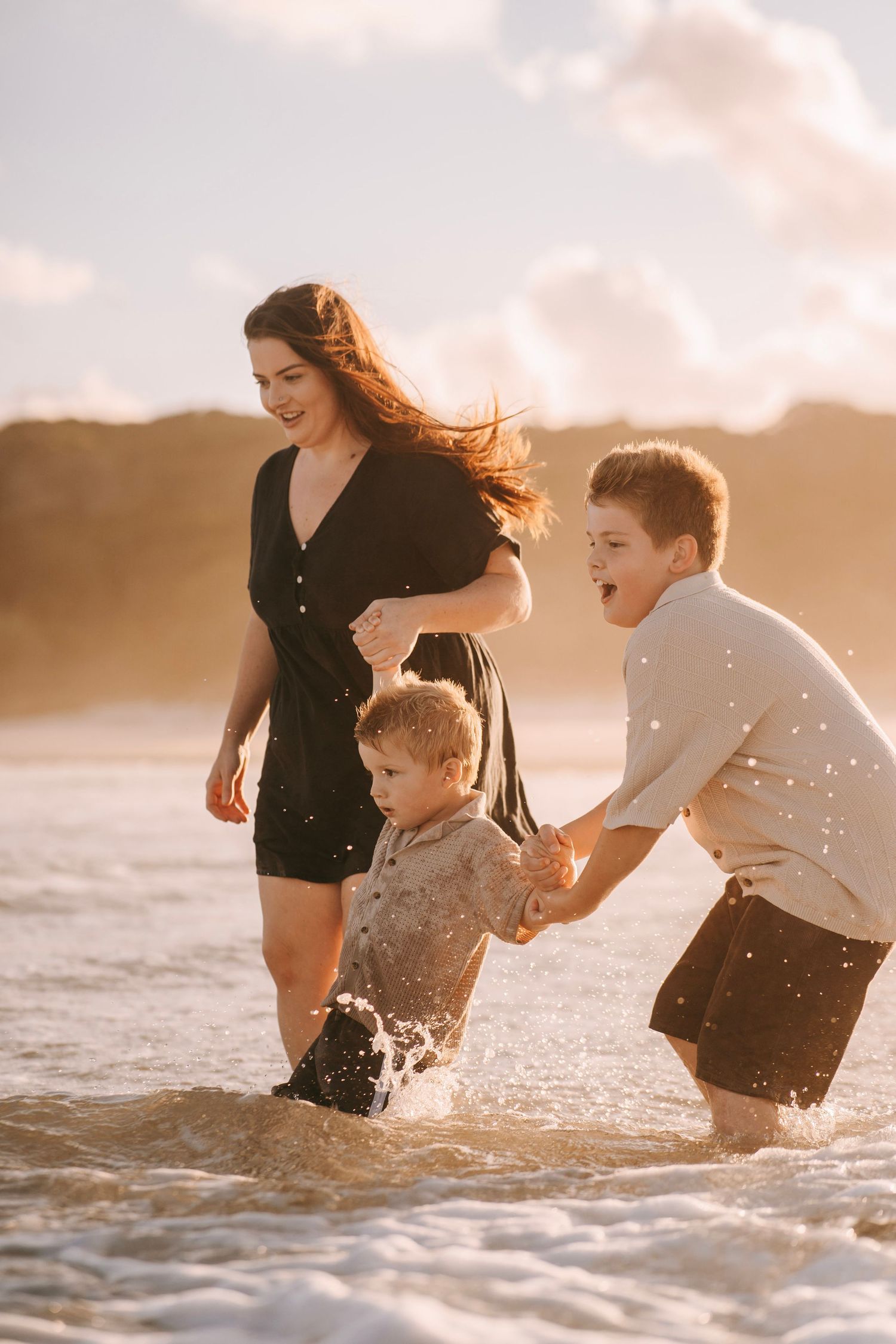 Mother and two boys playing in ocean waves at sunset, splashing and laughing together.