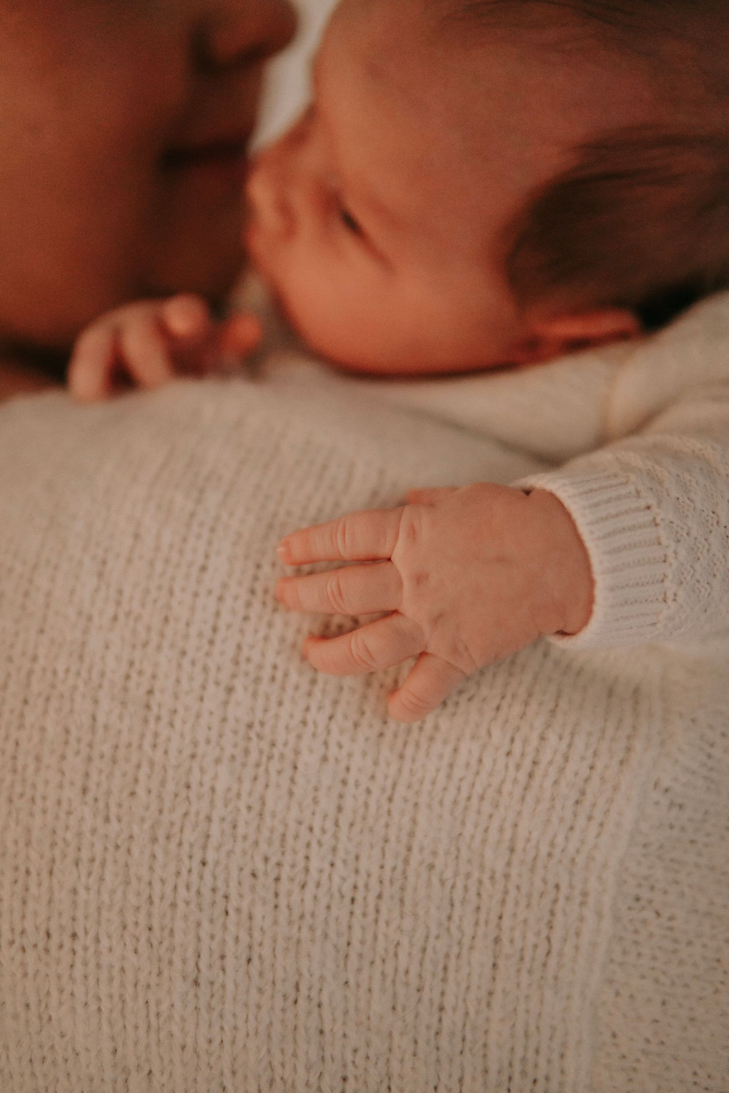 Detailed close-up of newborn babys tiny hand resting on mothers white knit sweater.
