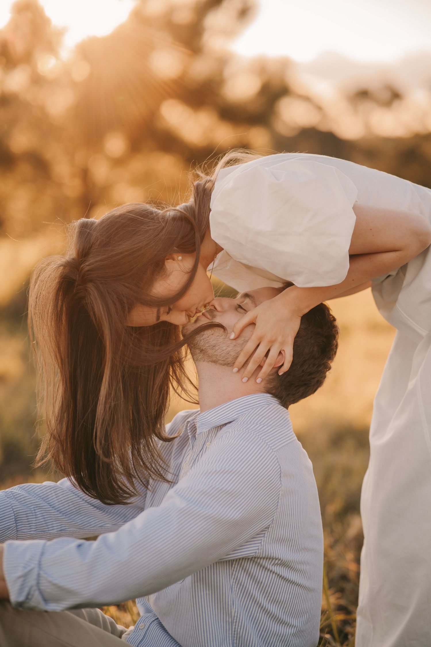 A couple sharing a romantic kiss in a sun-drenched golden field during sunset.