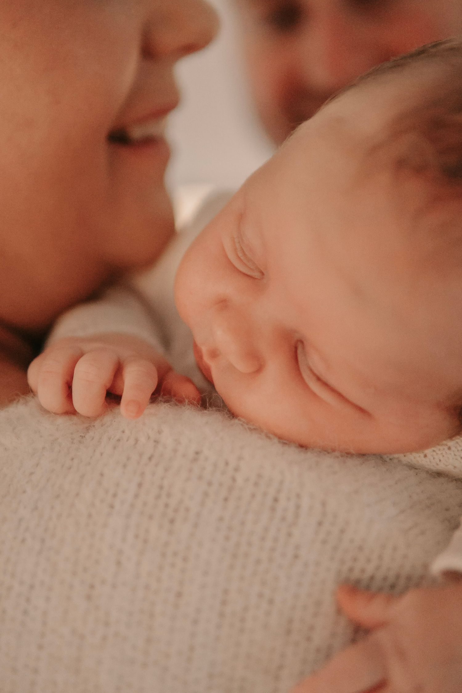 Close-up of sleeping newborn baby resting on mothers shoulder with tiny hands visible.