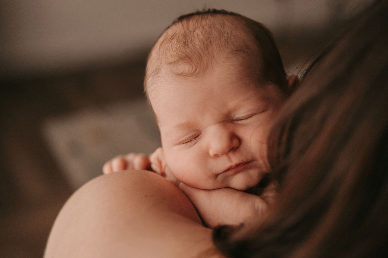 Peaceful newborn baby sleeping on parent's shoulder in warm, soft-lit portrait photography.