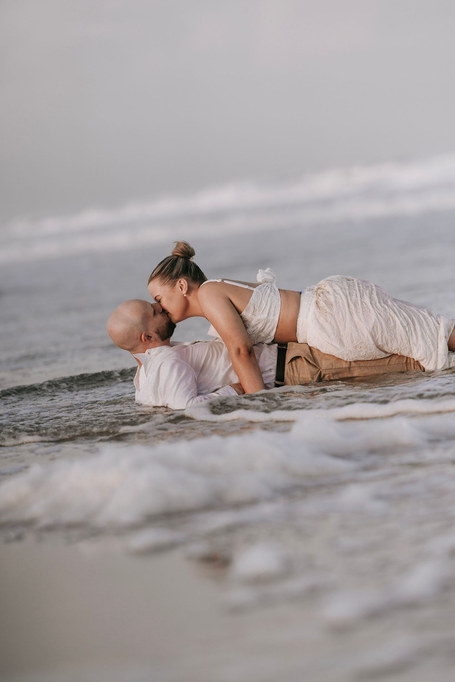 Couple sharing a passionate kiss while lying in shallow ocean waves on the beach.