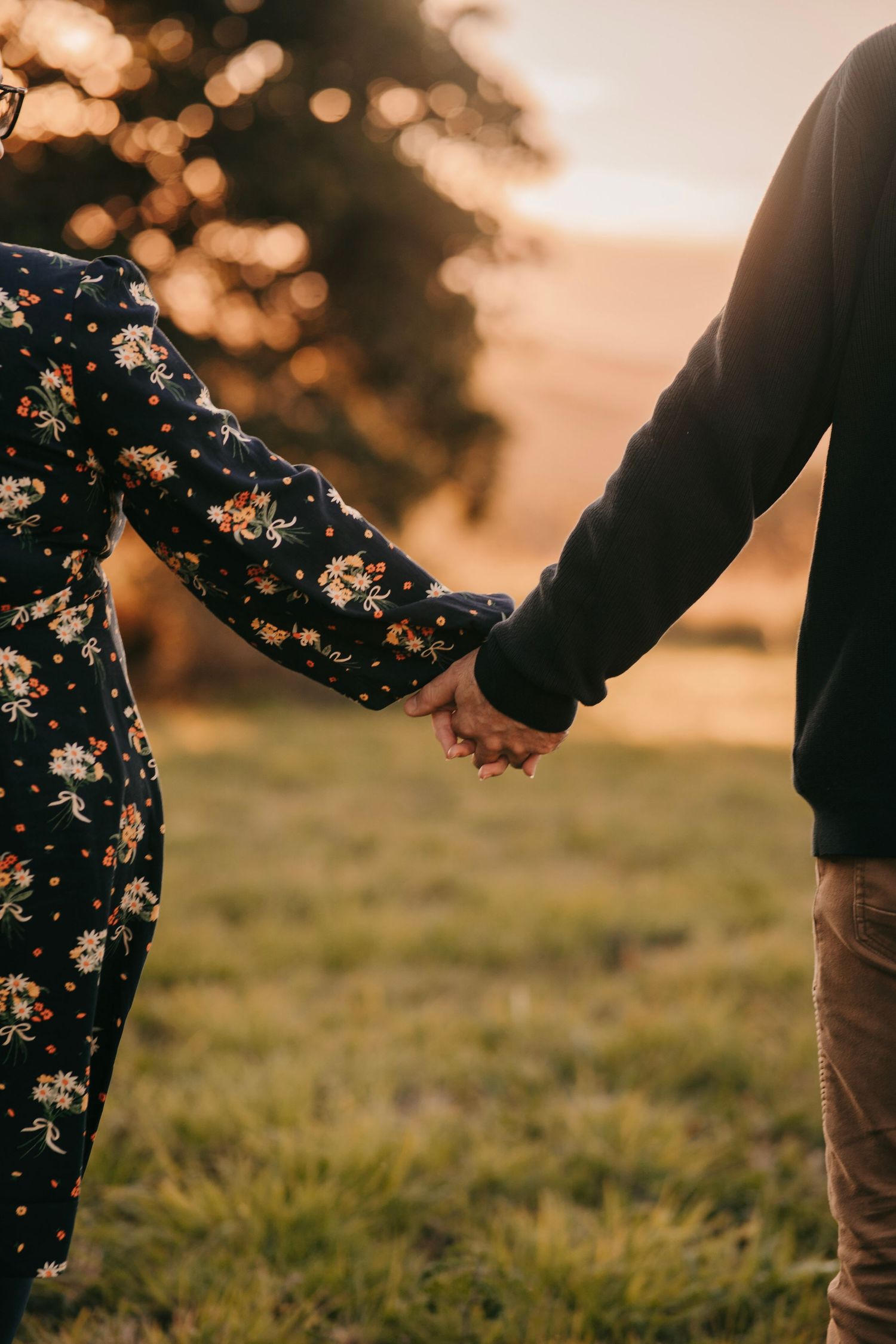 Couple holding hands in a field at sunset, woman wearing a floral dress.