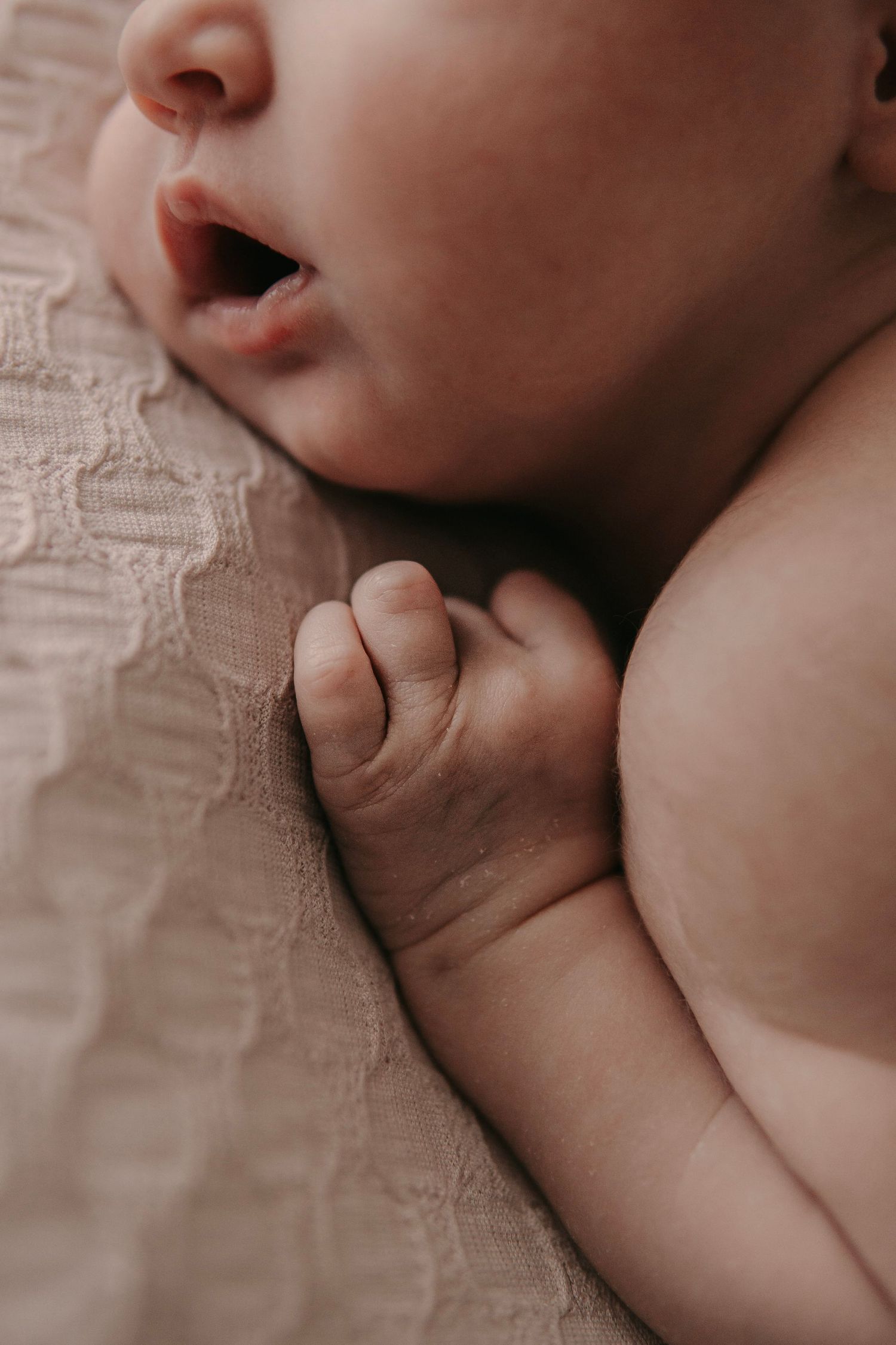Close-up of a peaceful newborn baby's face and tiny hand resting on a soft lace blanket.