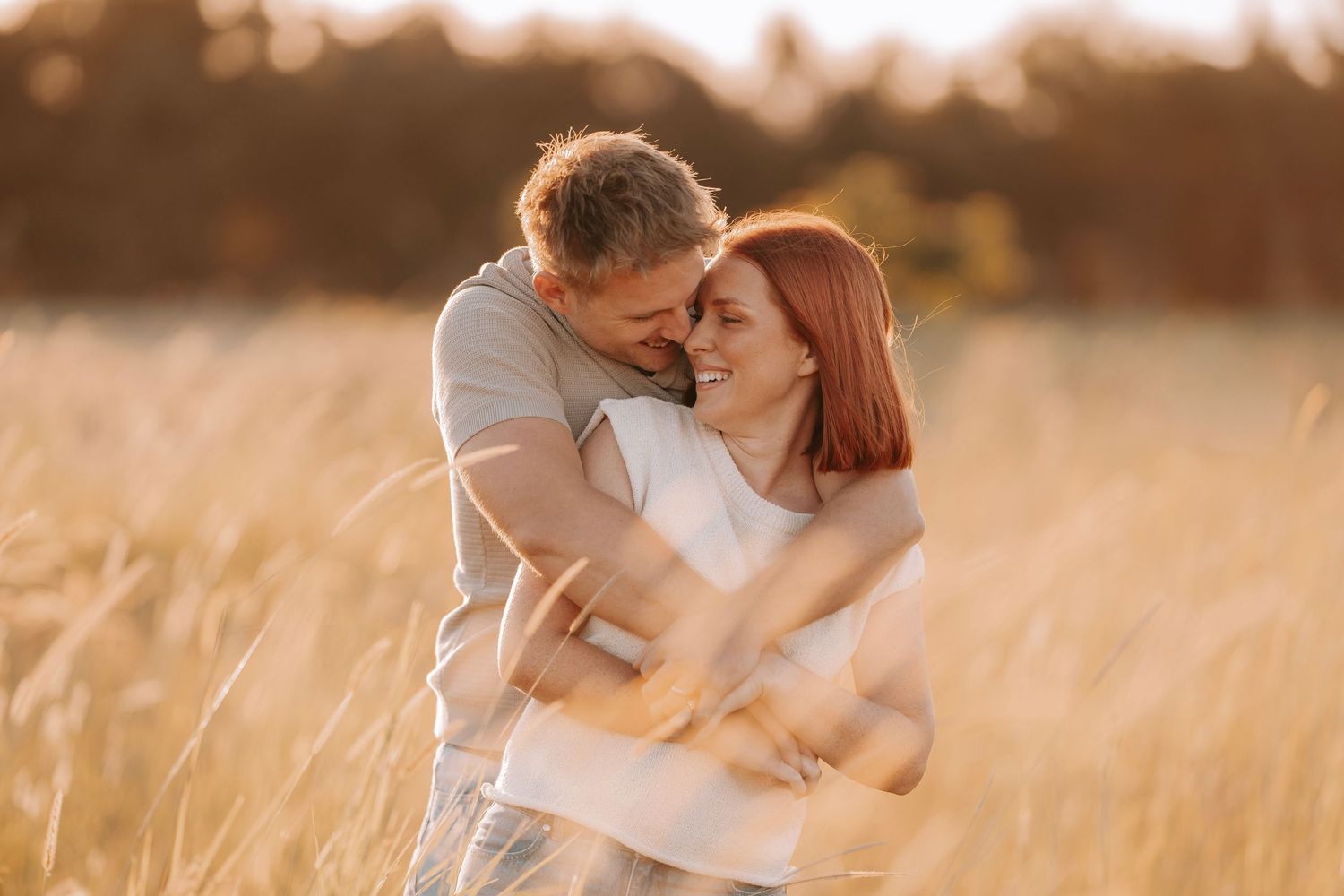 Happy couple embracing in a golden wheat field during sunset, sharing a romantic moment outdoors.